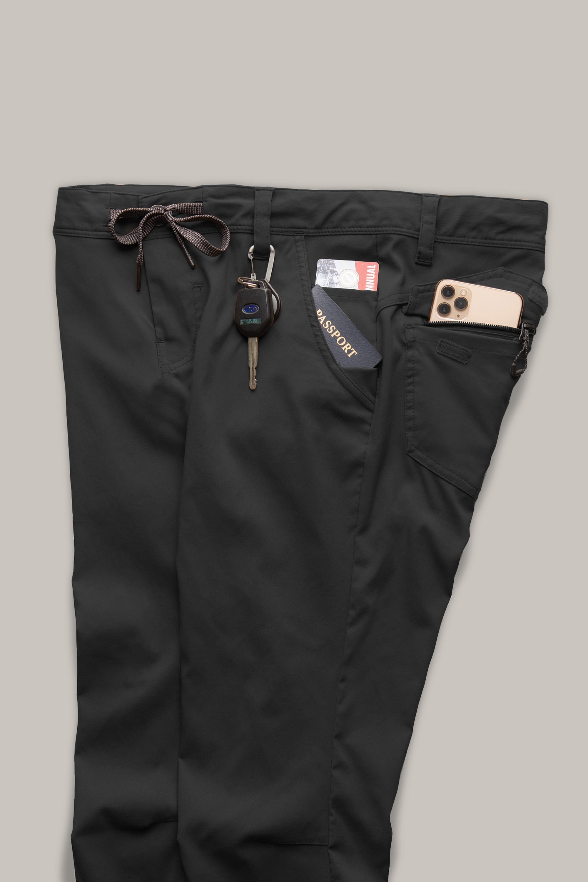 The 686 Mens Everywhere Ripstop Pant - Slim Fit by 686 in black features items placed in its pockets: a car key in the left, a passport and credit card in the right, and a smartphone partially in the zippered side pocket.
