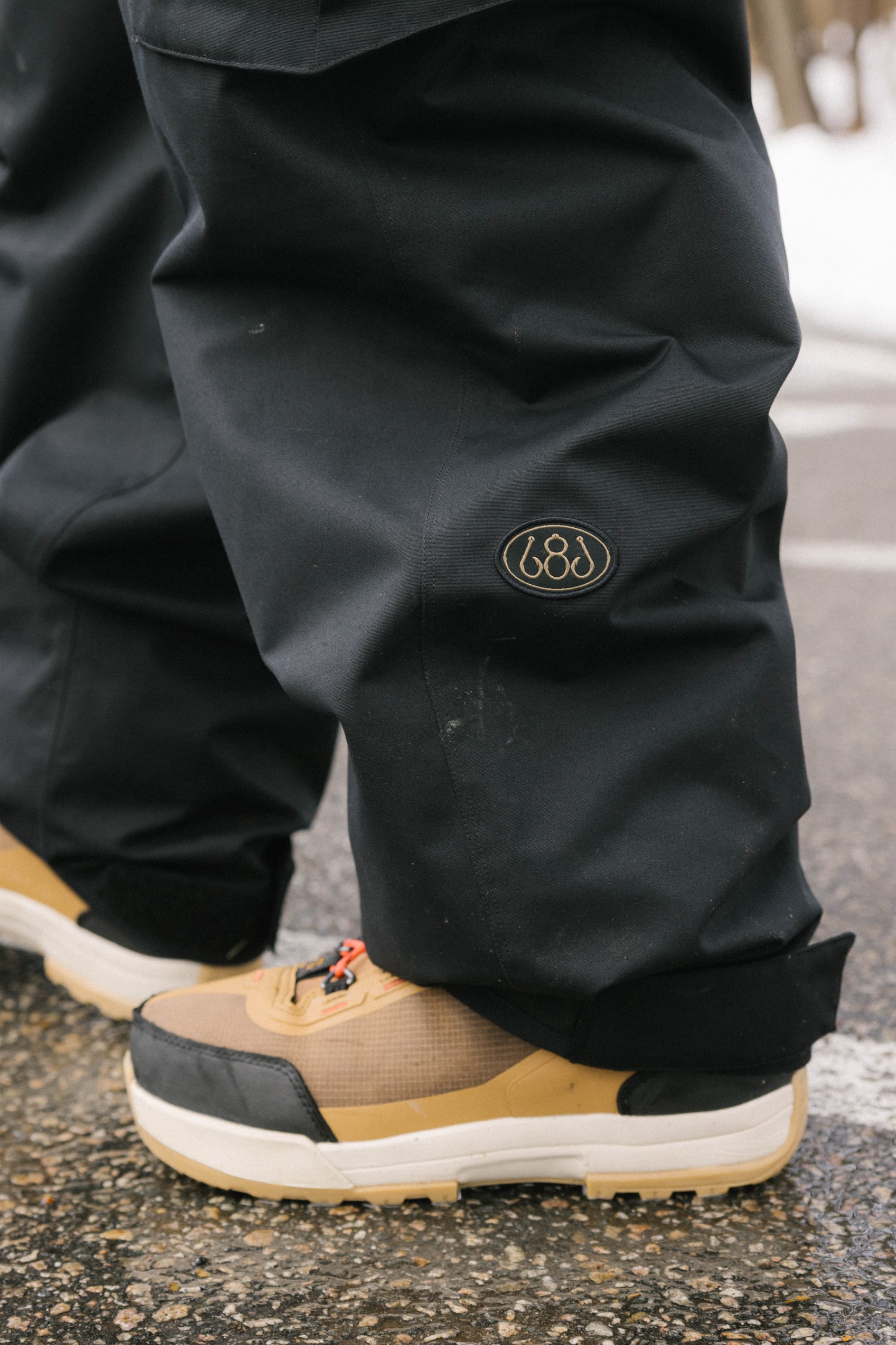 A person wearing the 686 Men’s Essox™ Cargo Pant and tan sneakers stands on a wet surface.