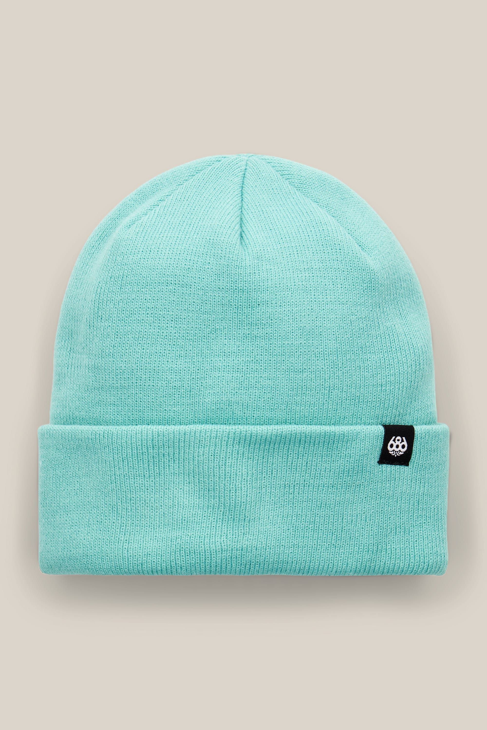 The 686 Standard Roll Up Beanie by 686 is a light turquoise knit hat featuring a folded brim and a small black rectangular tag with a white logo, shown against a neutral beige background.