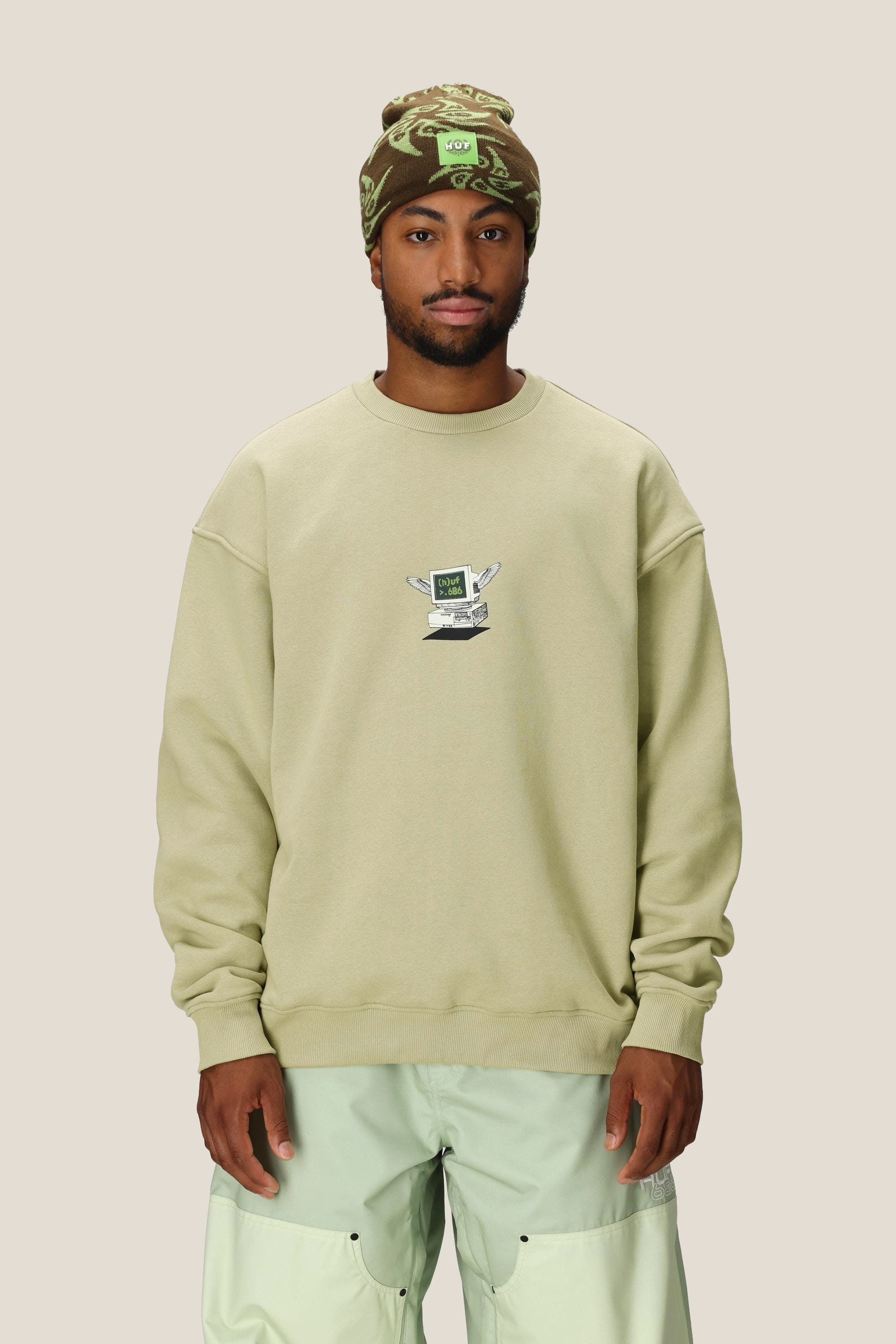 A man wearing a beige 686 HUF Premium Heavyweight Crew Sweatshirt by 686, mint green pants, and a green patterned beanie stands facing forward against a plain light background.