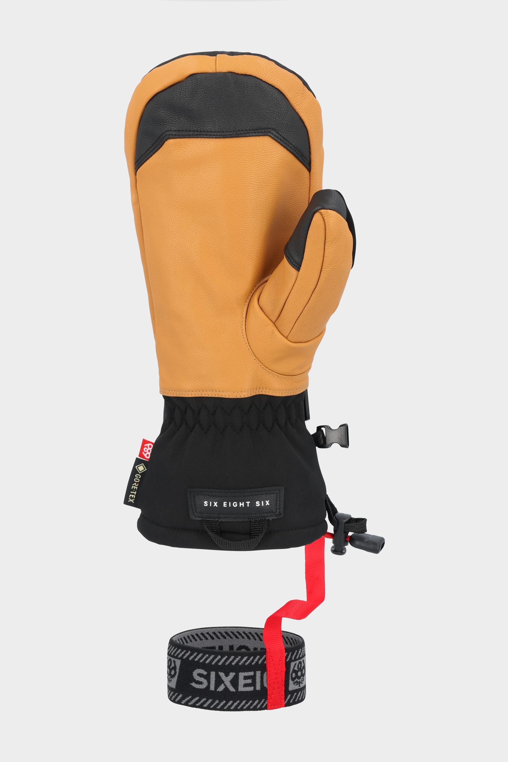 The 686 Mens GORE-TEX Leather Linear Mitt features tan and black woven material, an insulated leather palm, adjustable wrist strap, black elastic cuff, and a removable black and gray SIXEIGHT leash with red strap, shown on a white background.