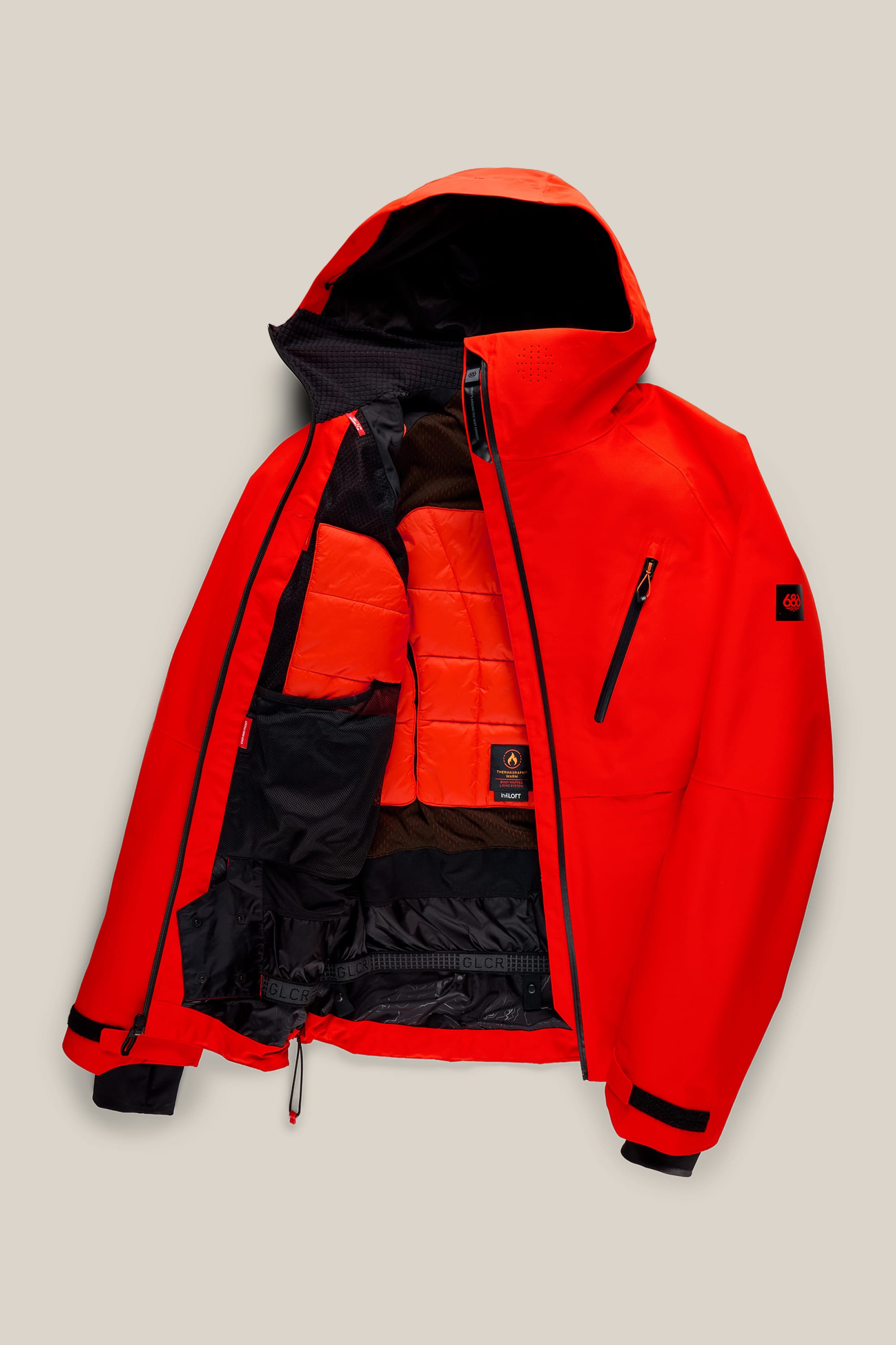 The 686 Men’s Hydra™ Thermagraph® Jacket by 686 is displayed on a beige background, unzipped to reveal its black and orange padded inner lining, zippered pockets, and inner mesh compartments.