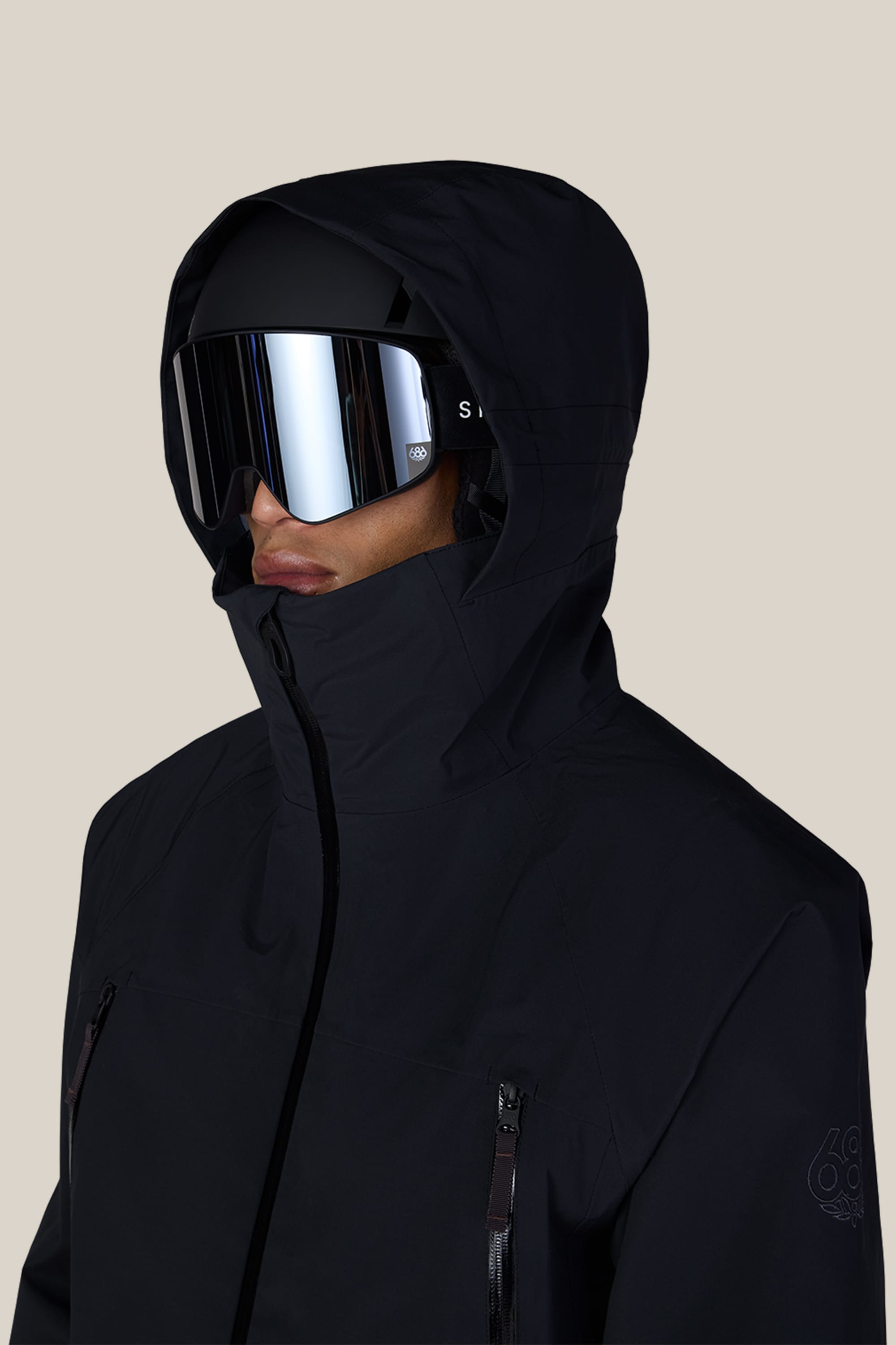 A man is wearing the 686 Men’s SMARTY® 3-In-1 Rodeo™ 3L Jacket in black and reflective ski goggles, facing slightly to the left against a plain beige background.