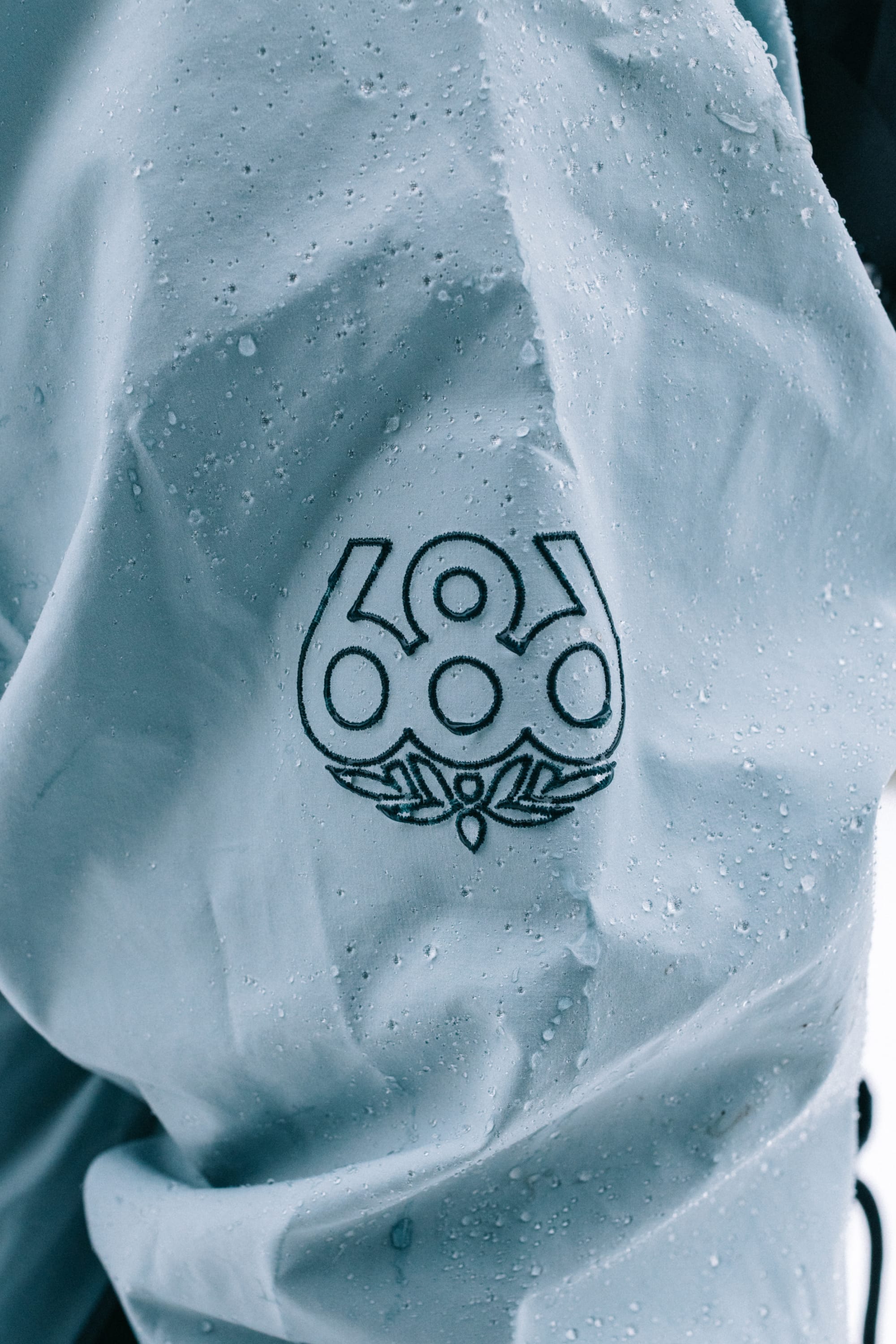 A close-up of the 686 Men’s SMARTY® 3-In-1 Rodeo™ 3L Jacket sleeve in light blue, featuring water droplets and an embroidered black 686 logo.