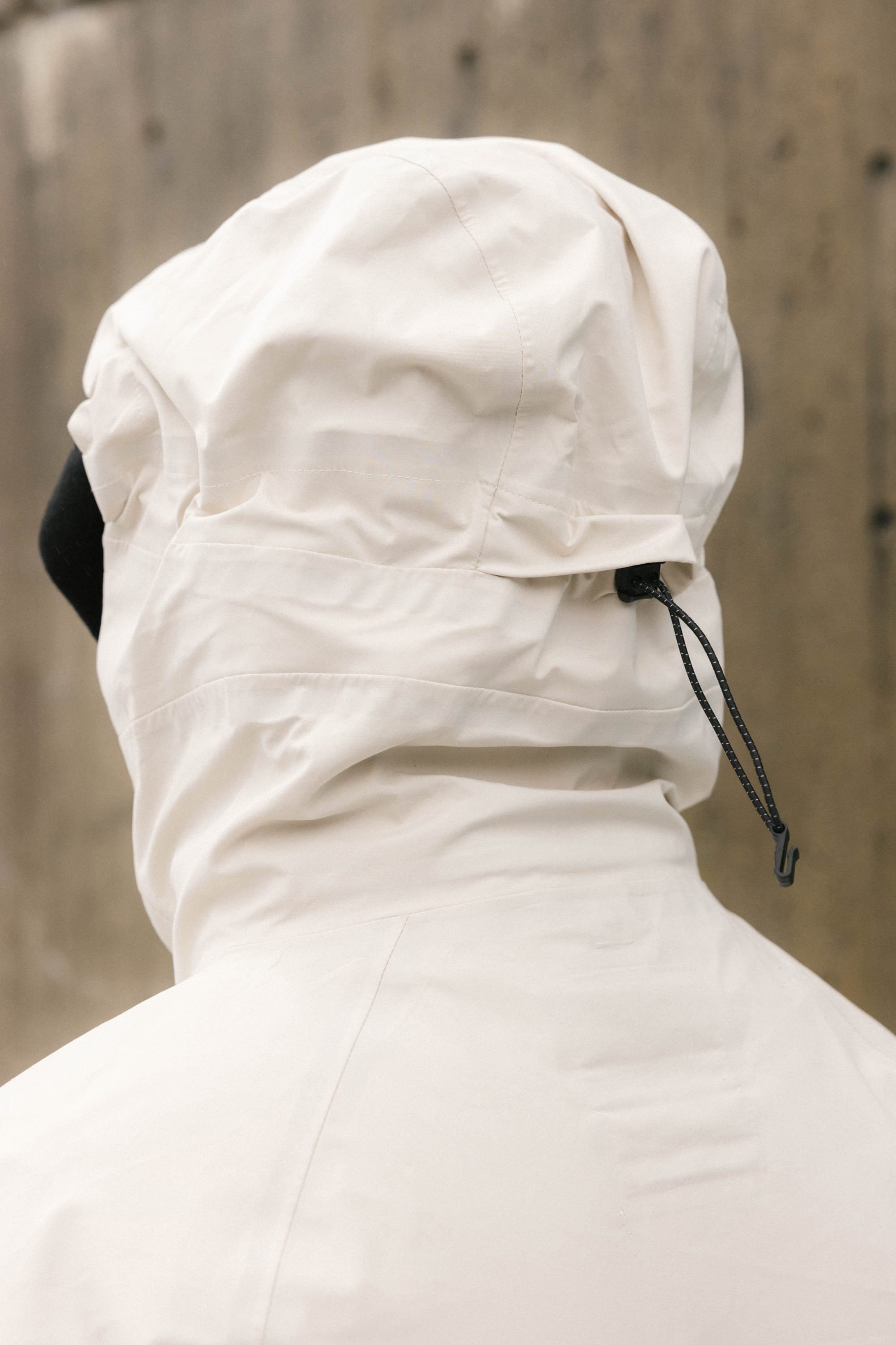 A person is seen from the back wearing the 686 Men’s SMARTY® 3-In-1 Rodeo™ 3L Jacket—a white hooded jacket with a black drawstring—set against a blurred, neutral-toned background.