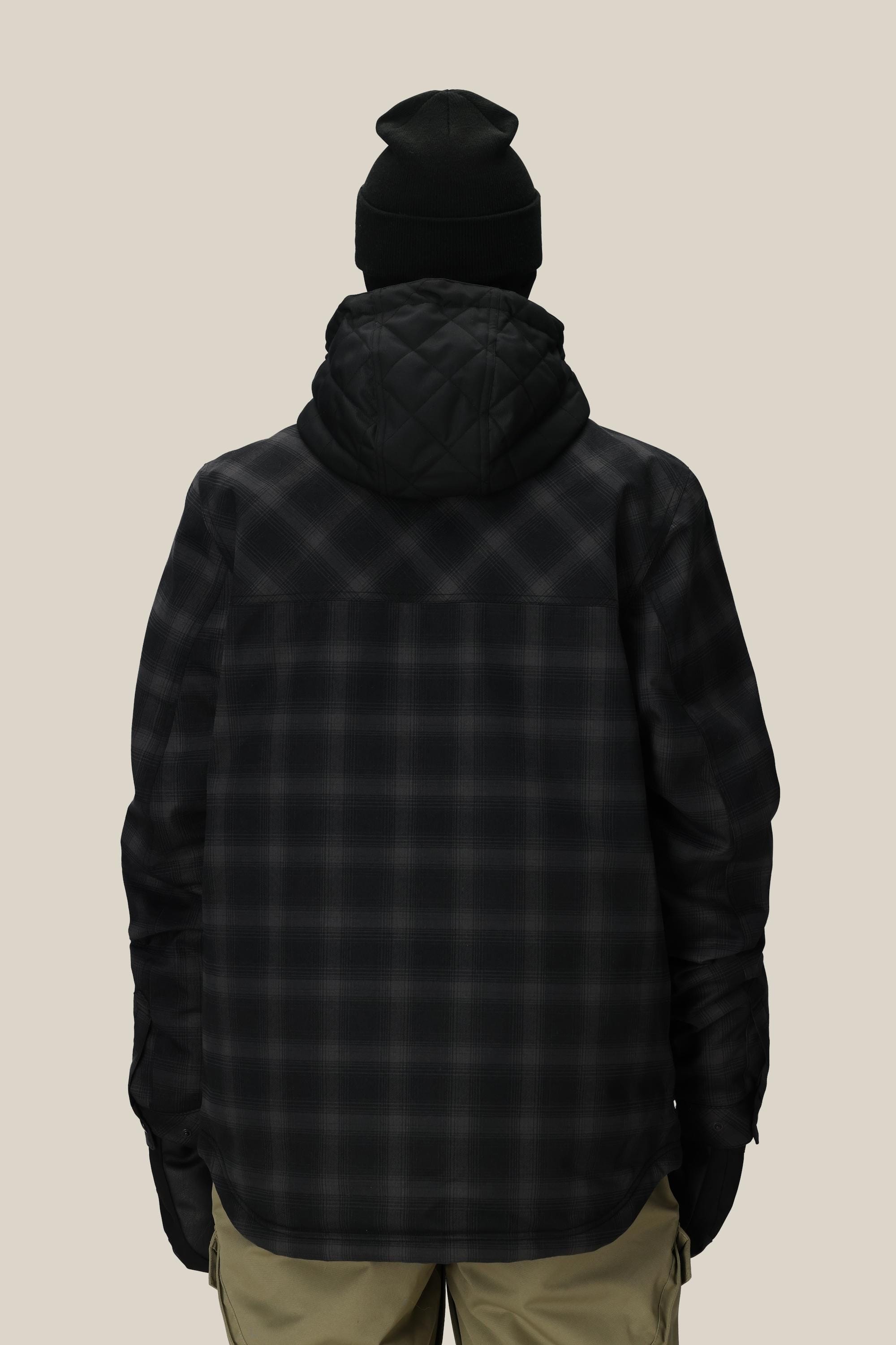 A person wearing a black beanie, khaki pants, and the 686 Mens Woodland Insulated Jacket, shown from the back against a plain light background.