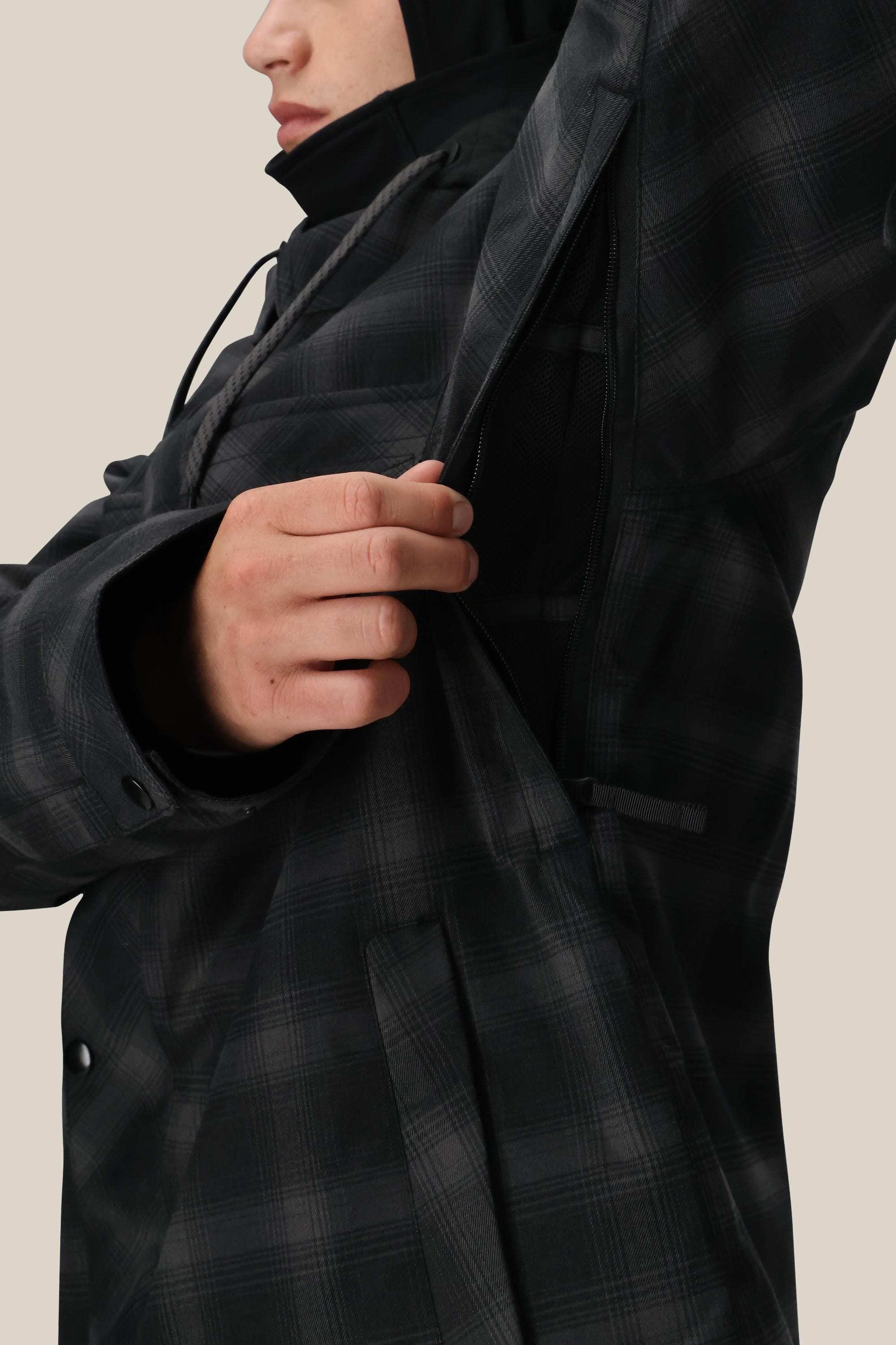 A man wearing the 686 Men’s Woodland Insulated Jacket unzips an underarm vent, revealing mesh lining. The image highlights his torso and hand, with his face partially visible.