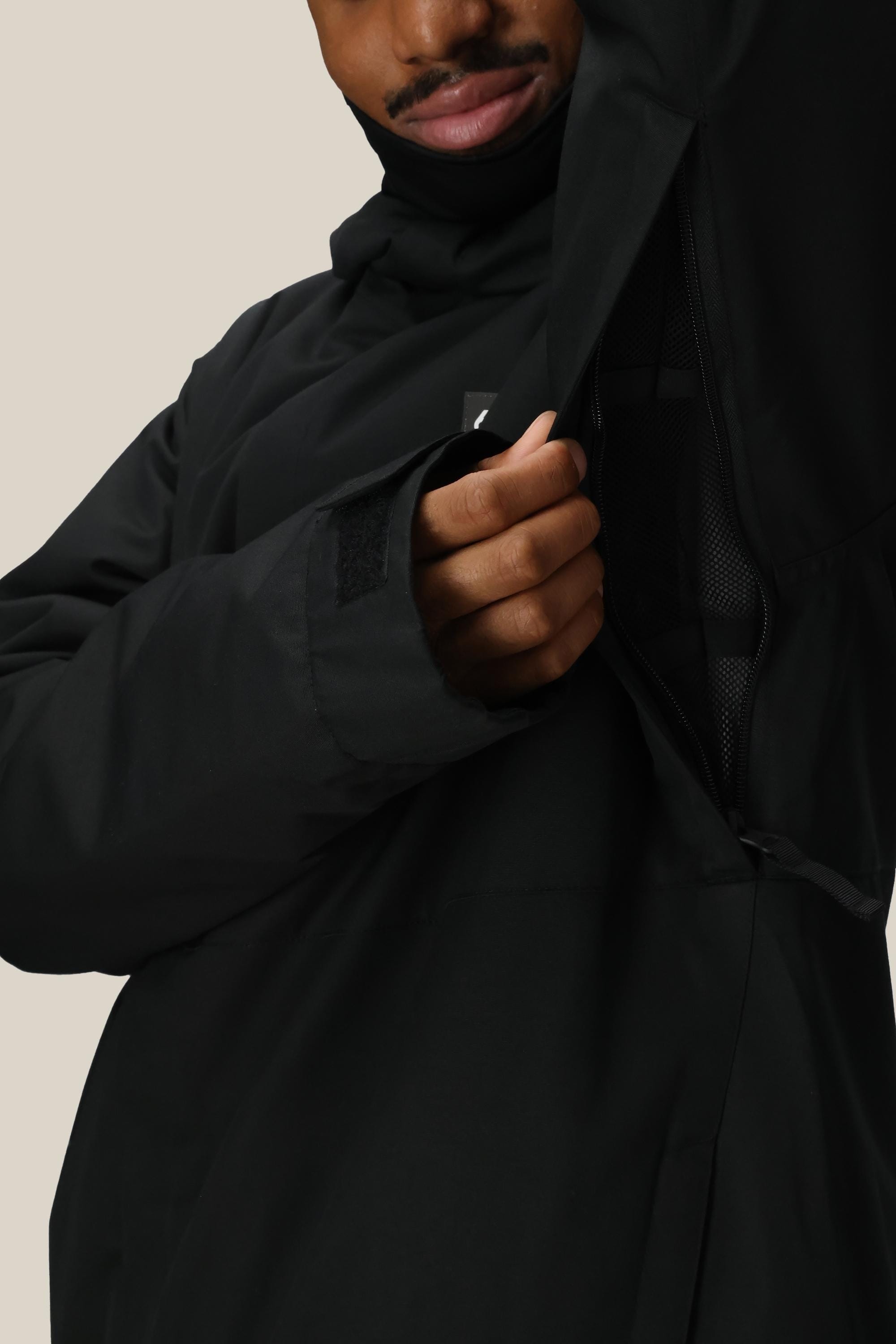 A man in a 686 Mens Foundation Insulated Jacket unzips a side vent, showing the mesh lining and thumb holes in the sleeve. He stands against a plain, light-colored background.