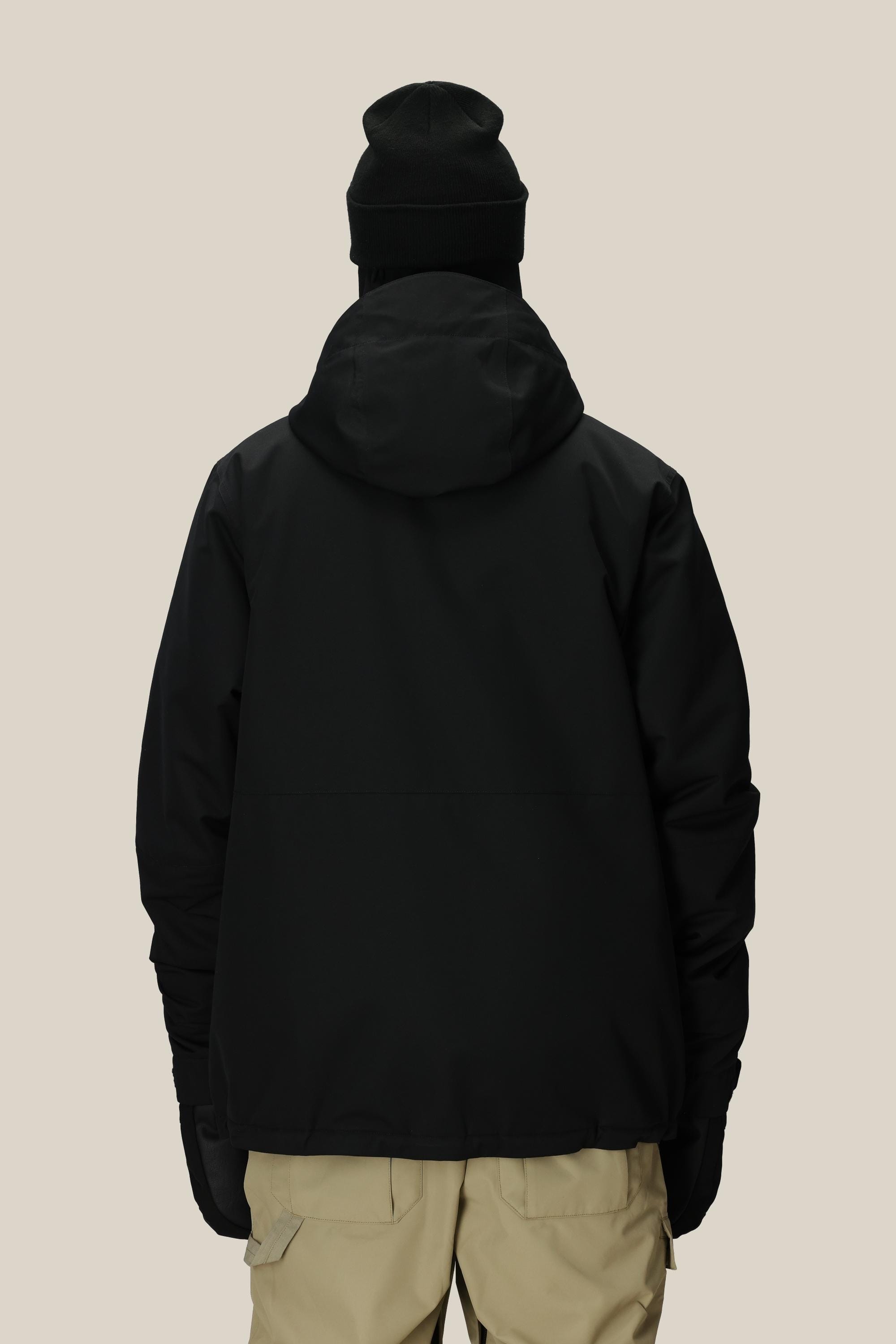 A person wearing a 686 Mens Foundation Insulated Jacket in black, along with a black beanie and beige pants, stands facing away from the camera against a plain light background.