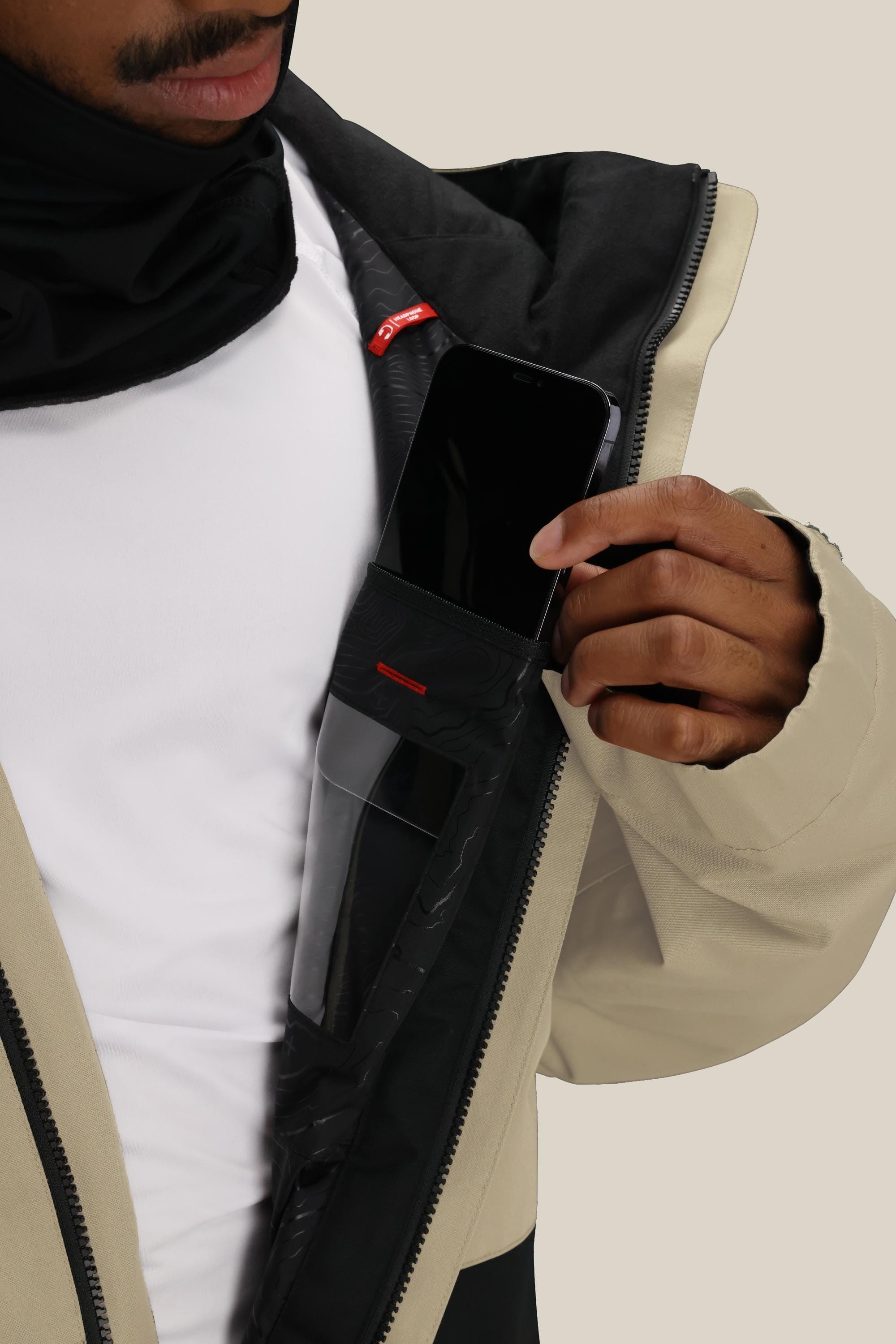 A person, with only the lower part of their face visible, places a smartphone into the inner zippered pocket of the 686 Mens Foundation Insulated Jacket, showcasing this 686 jackets secure storage feature.
