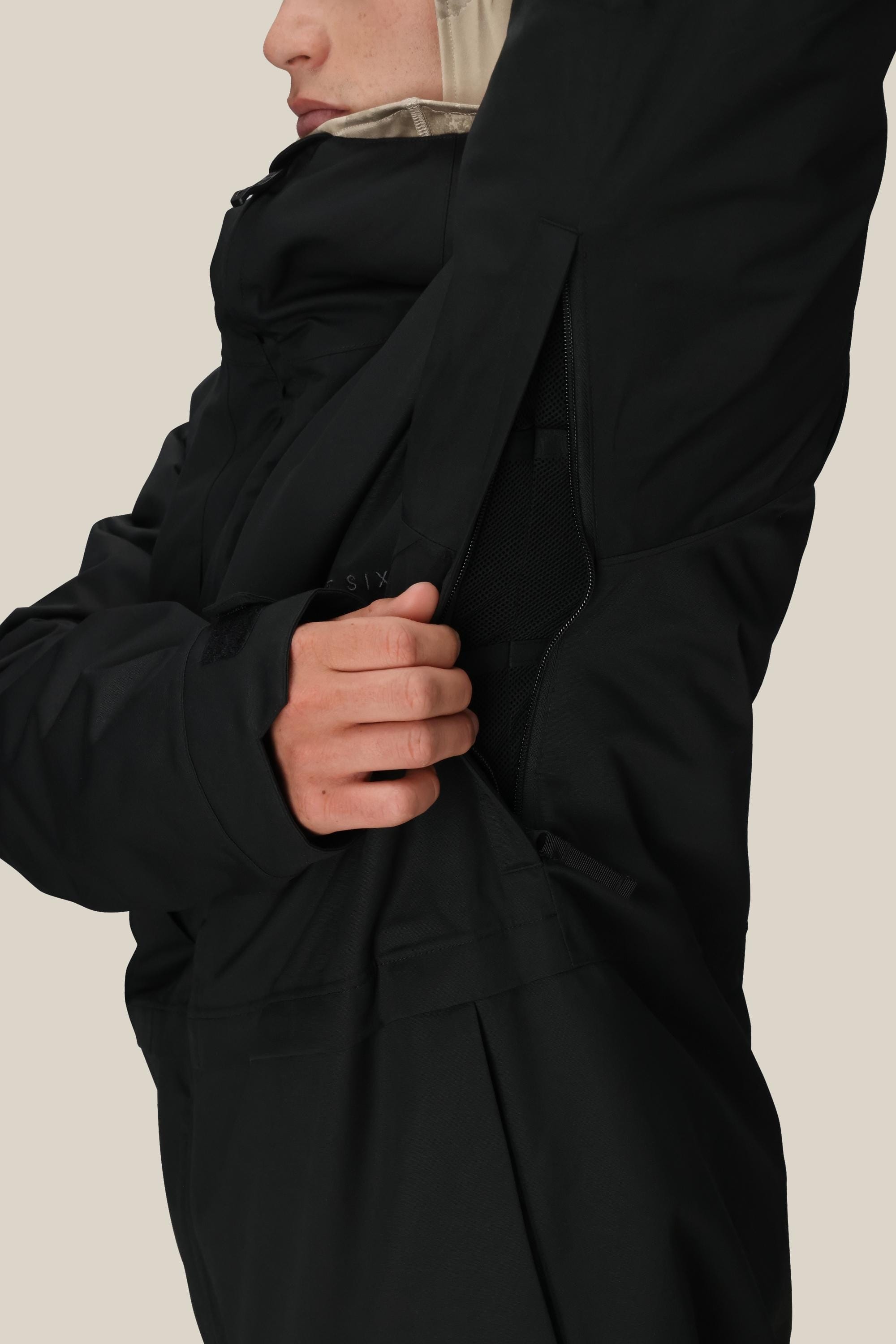 A person wearing the 686 Mens Smarty 3-In-1 Form Jacket unzips an underarm vent, showing mesh lining beneath. The plain, neutral background highlights the black jacket by 686.