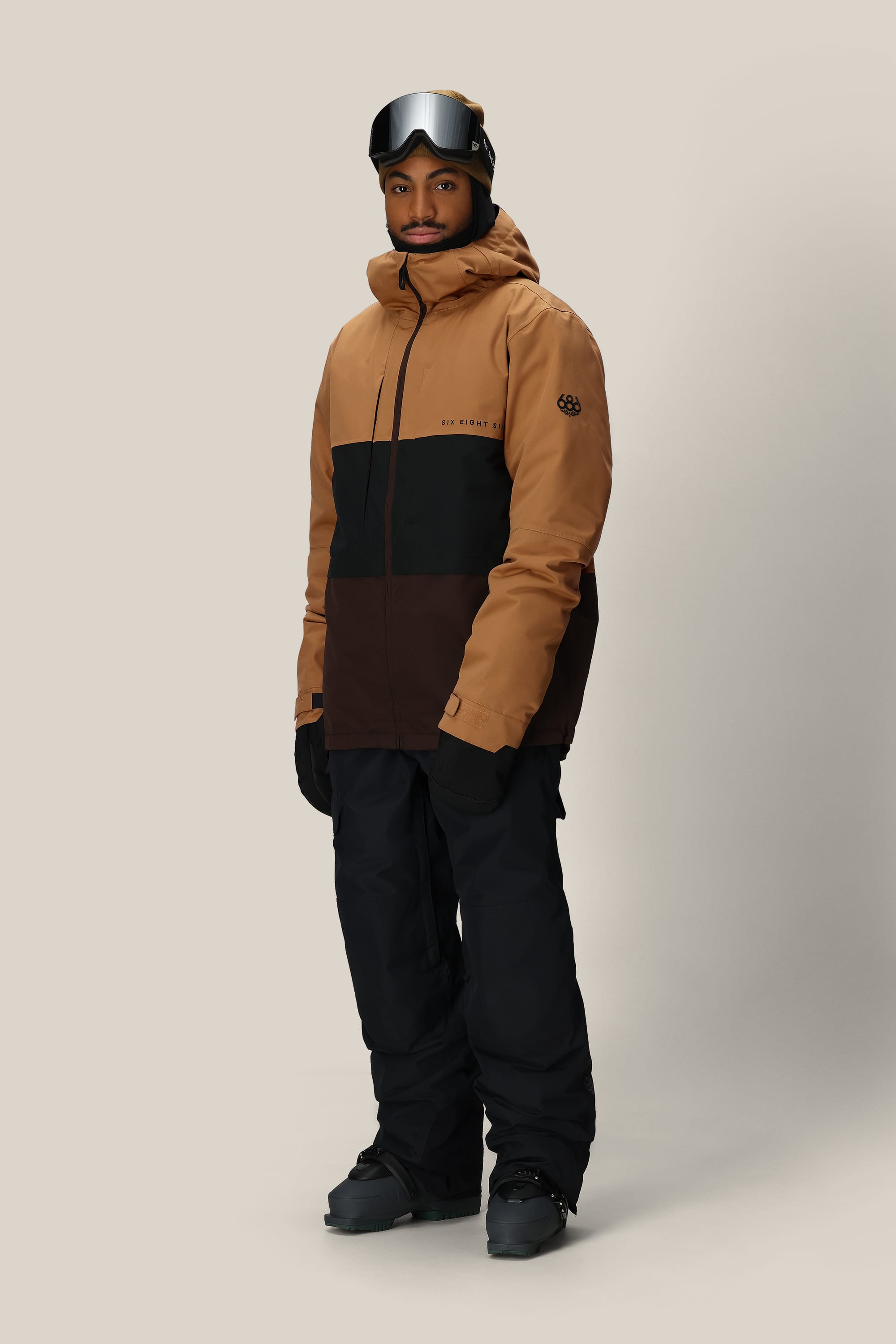 A person in the 686 Mens Smarty 3-In-1 Form Jacket by 686, paired with black snow pants, gloves, boots, and ski goggles, stands against a light gray background.