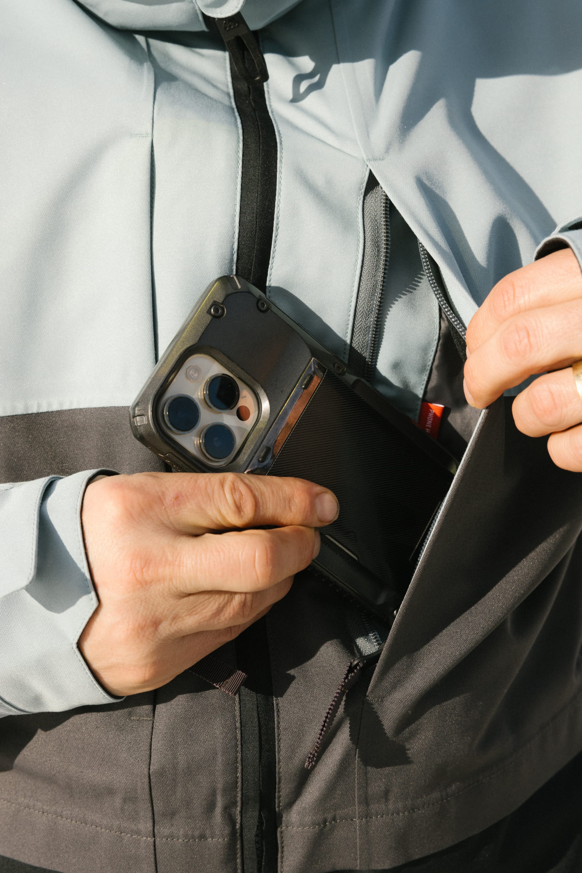 A man wearing the 686 Mens Smarty 3-In-1 Form Jacket slips a smartphone with a rugged case into the jacket’s zippered pocket.