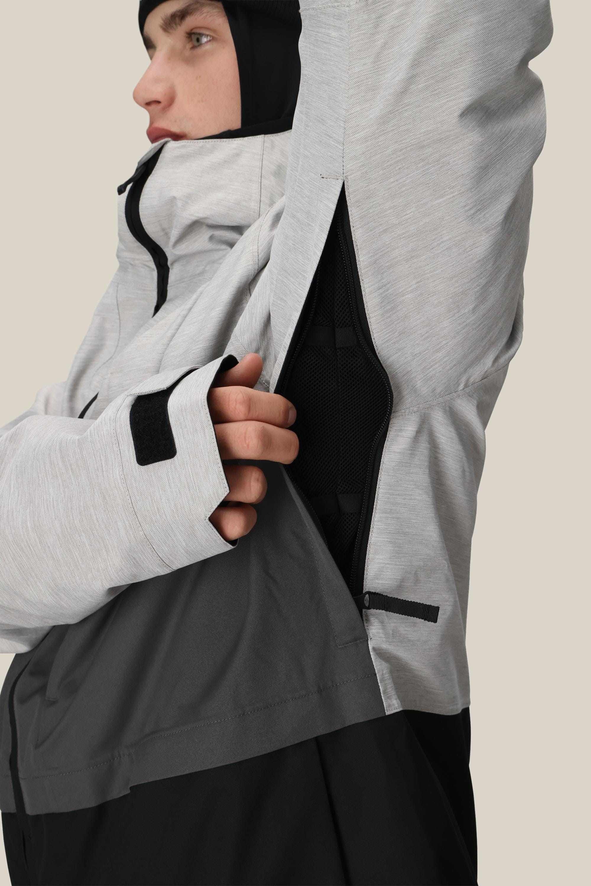 A person wearing the 686 Mens Smarty 3-In-1 Form Jacket in light gray with a black hood unzips a side vent under the arm, showing its mesh lining. The 686 jacket also features a woven design and thumb hole on the sleeve.