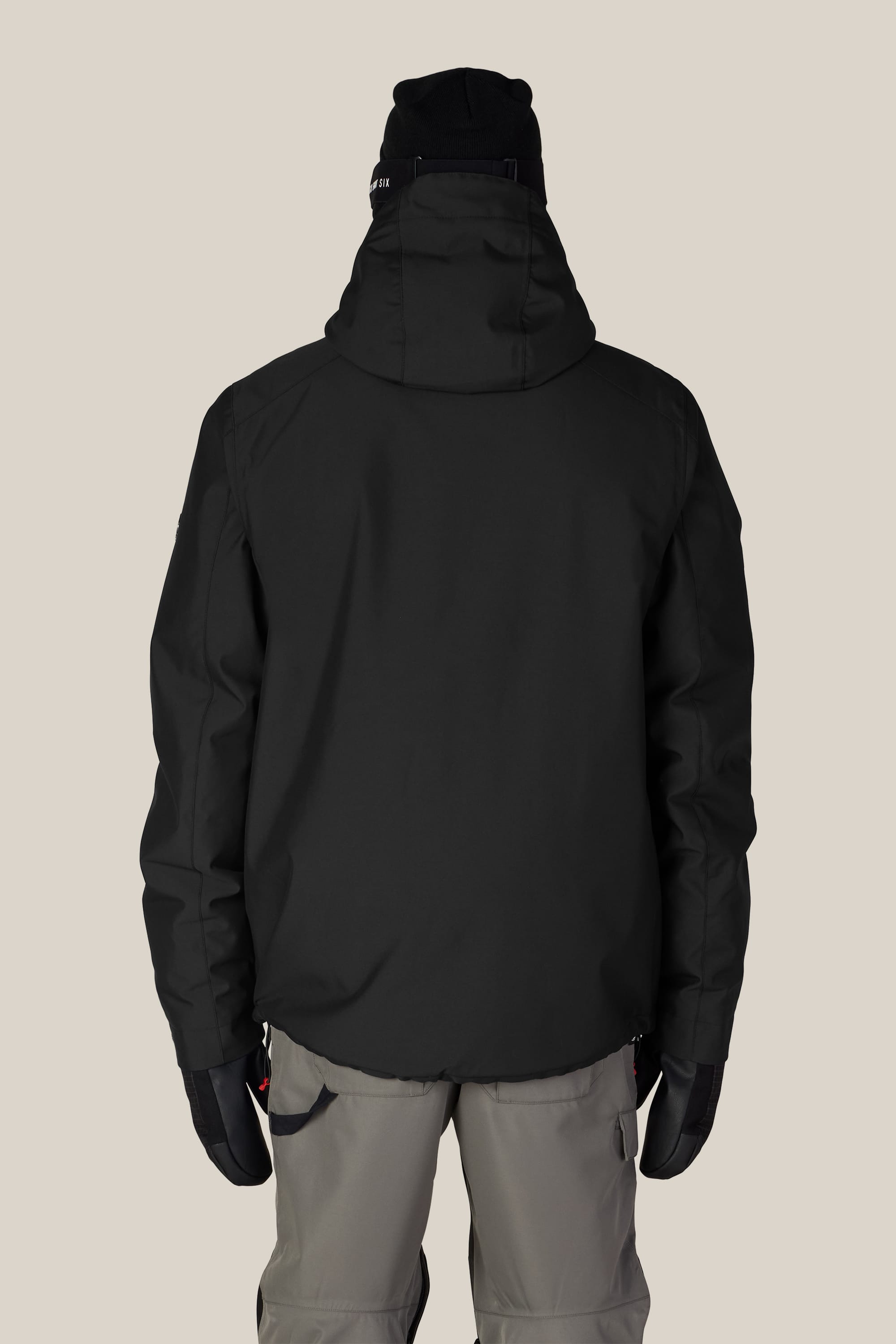 A person wearing the 686 Men’s Nightline™ Insulated Jacket by 686, along with black gloves and gray pants, is standing with their back to the camera against a beige background.