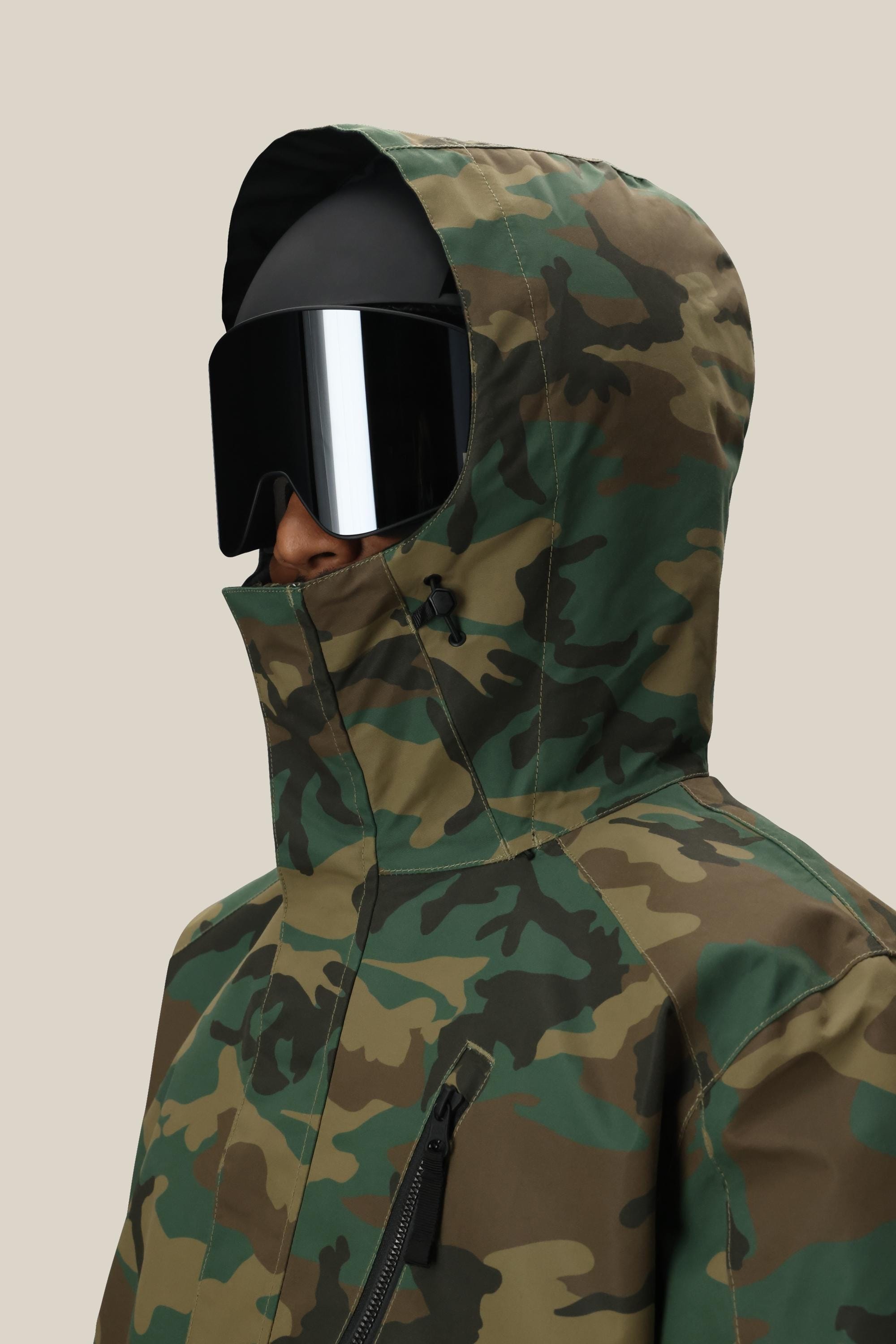 A person wearing the 686 Men’s Nightline™ Insulated Jacket by 686, styled with black ski goggles and a black helmet, facing left against a plain beige background.