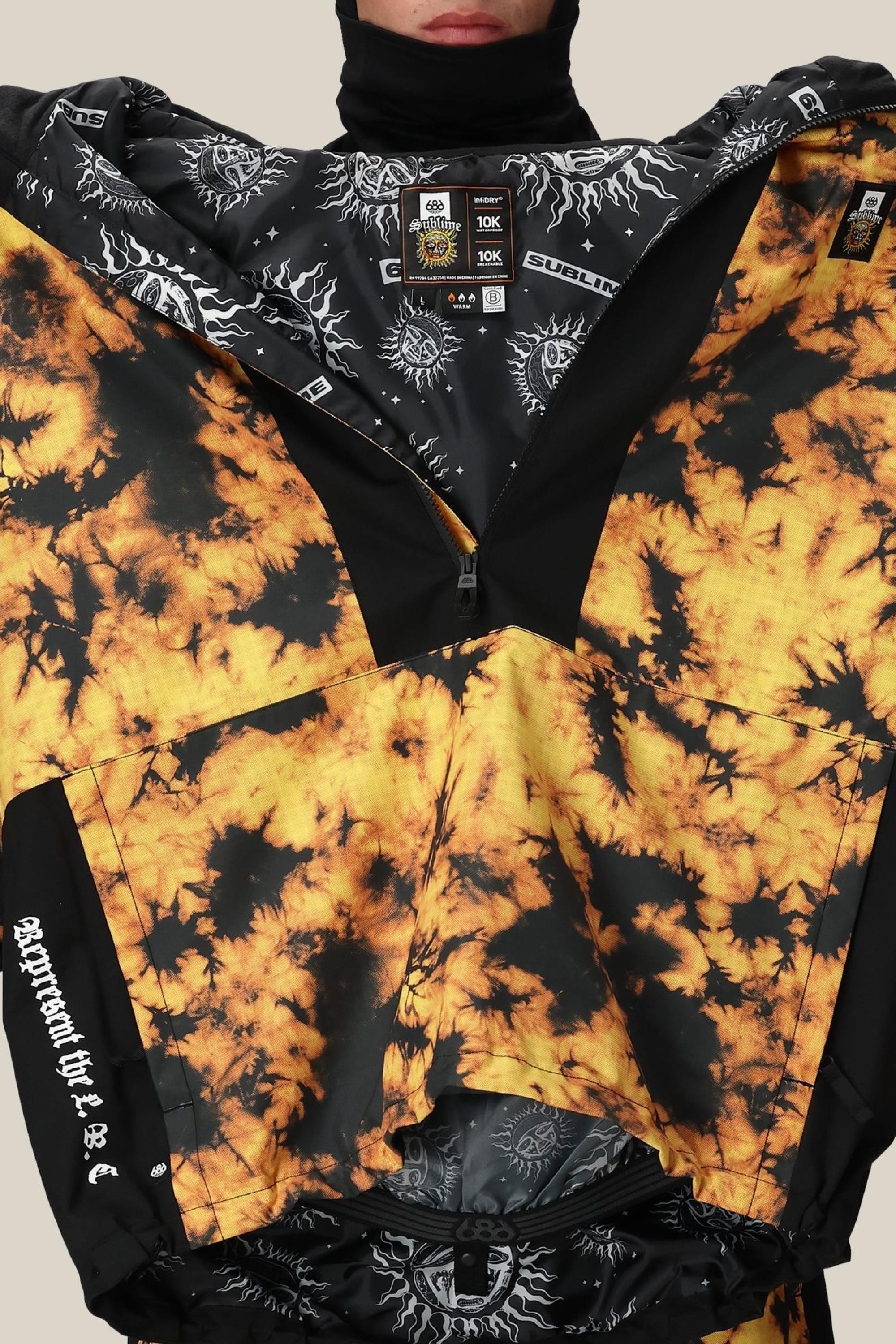 A person wearing the 686 Mens Sublime Shell Anorak—a high-collared black and yellow jacket with visible neck labels, white text, black printed lining, and a durable polyester waterproof build by 686.
