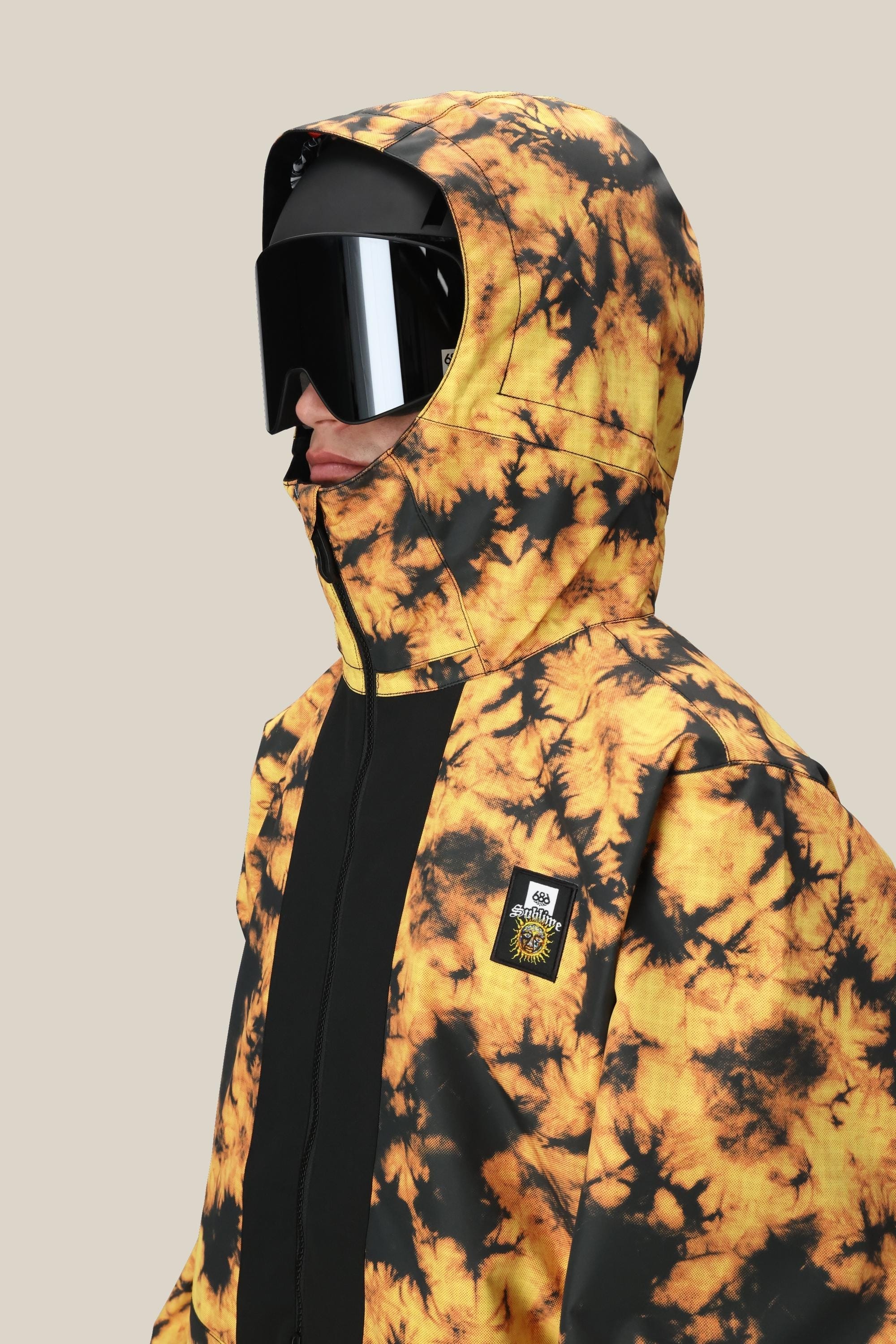 A man in the 686 Mens Sublime Shell Anorak (yellow and black) with the hood up, black ski goggles, and a face covering is photographed from the side against a plain beige background.