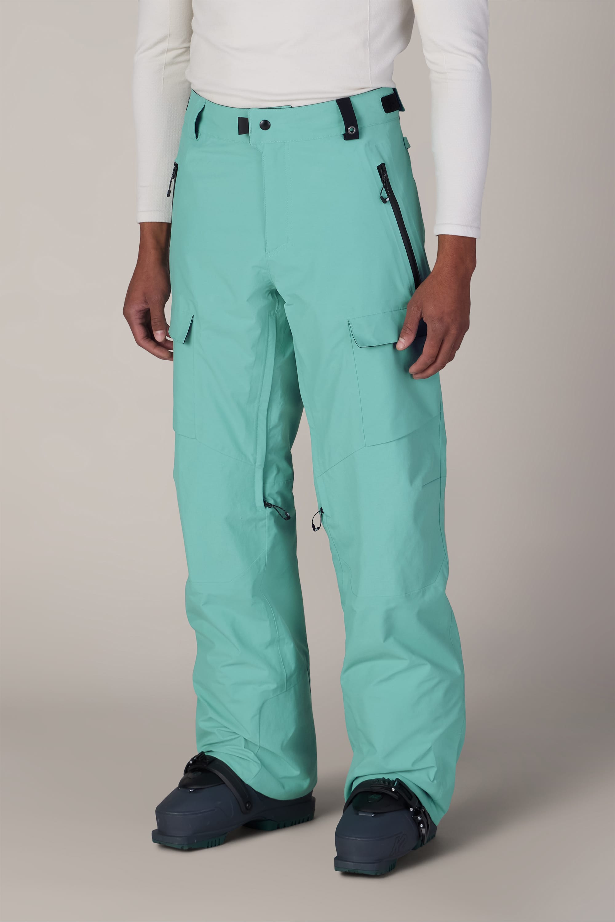 A person wearing 686 Men’s GORE-TEX® Dispatch™ Shell Pant by 686, paired with a white long-sleeve shirt and black snow boots, stands against a neutral background.