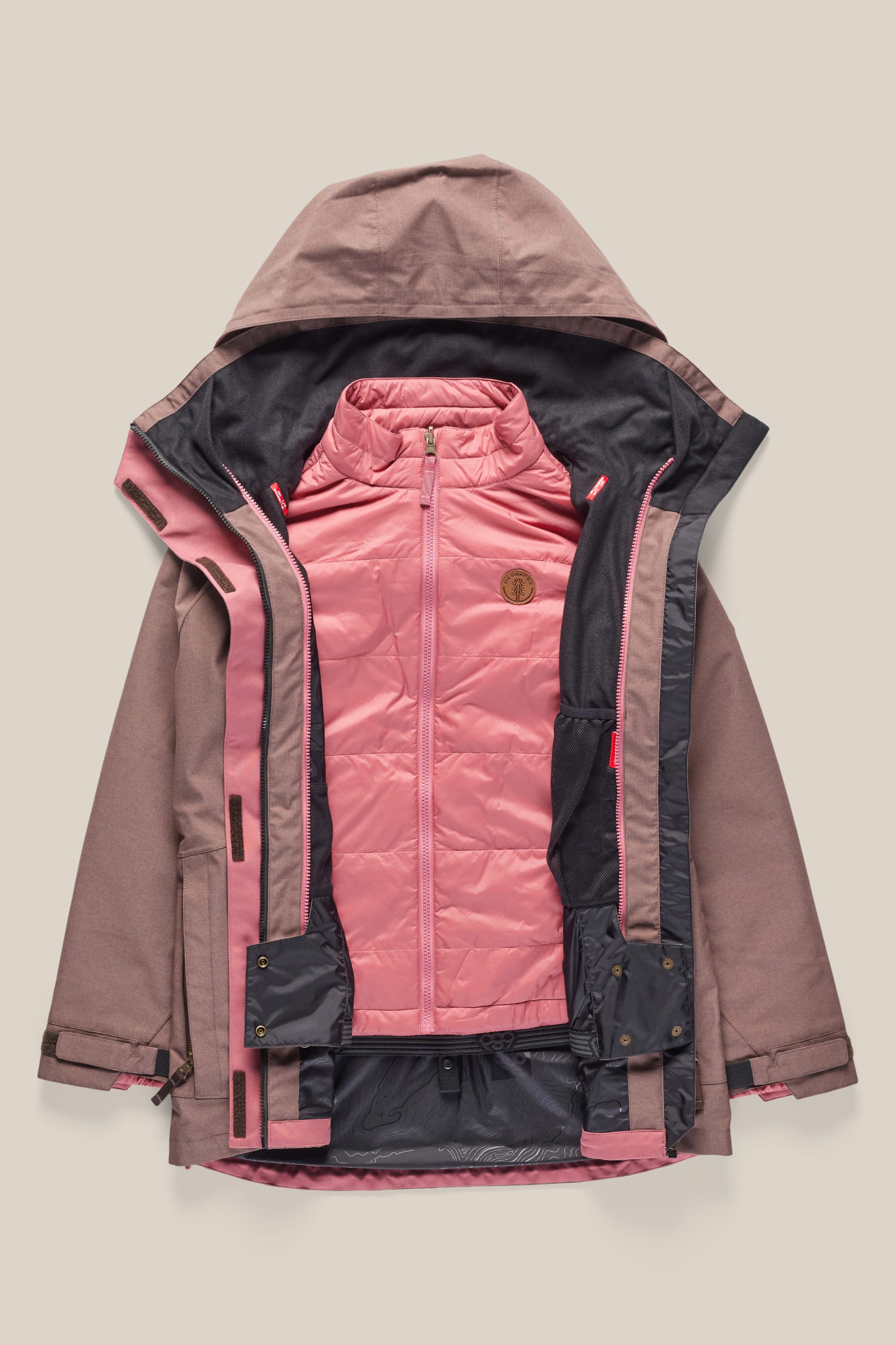 The 686 Womens Smarty 3-In-1 Spellbound Jacket by 686 features a mauve waterproof outer shell with a hood and an unzipped front revealing a detachable quilted light pink inner jacket with a stand-up collar and chest patch for versatile wear.