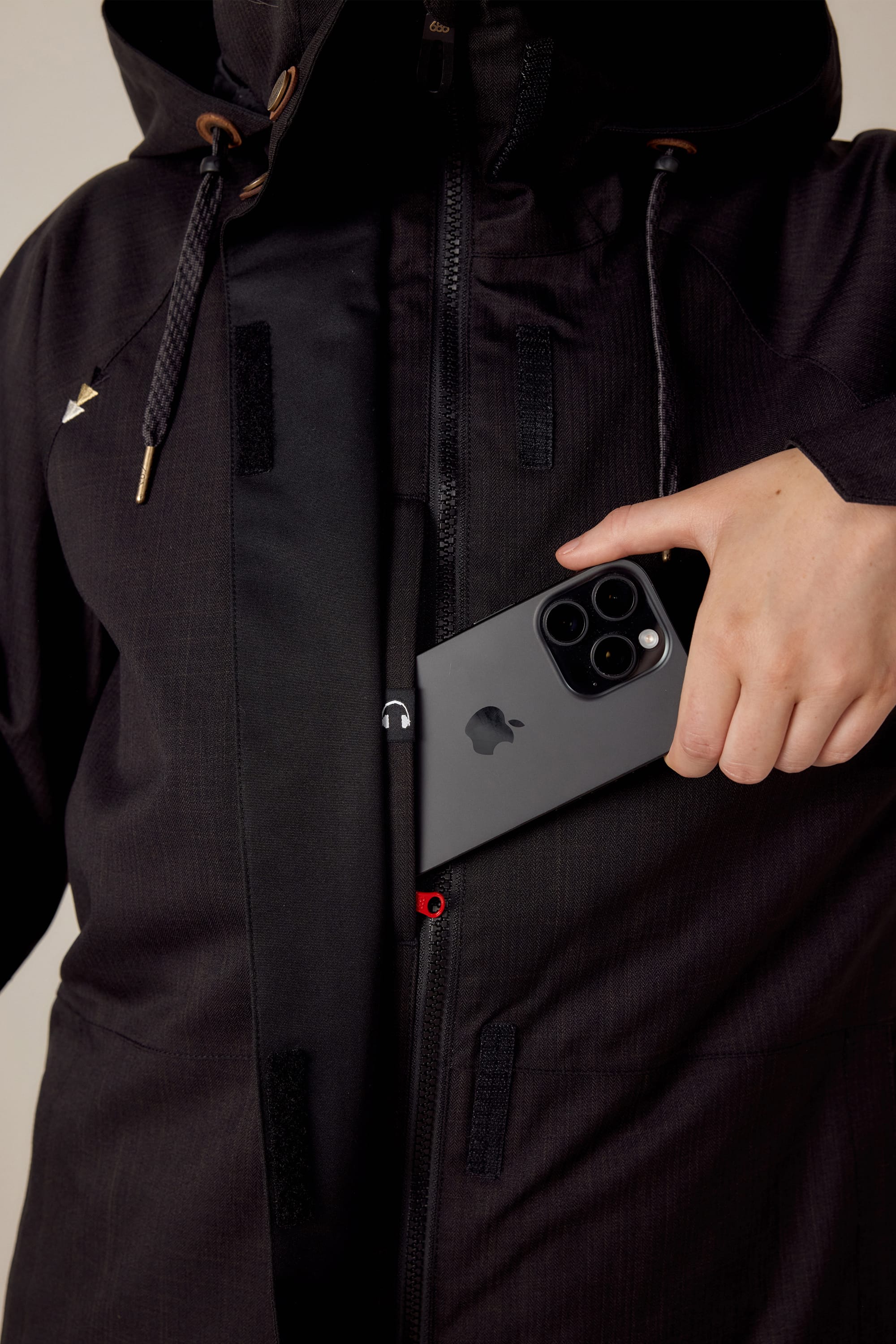 A woman unzips her 686 Womens Smarty 3-In-1 Spellbound Jacket and puts a black iPhone with three cameras into its inner pocket.