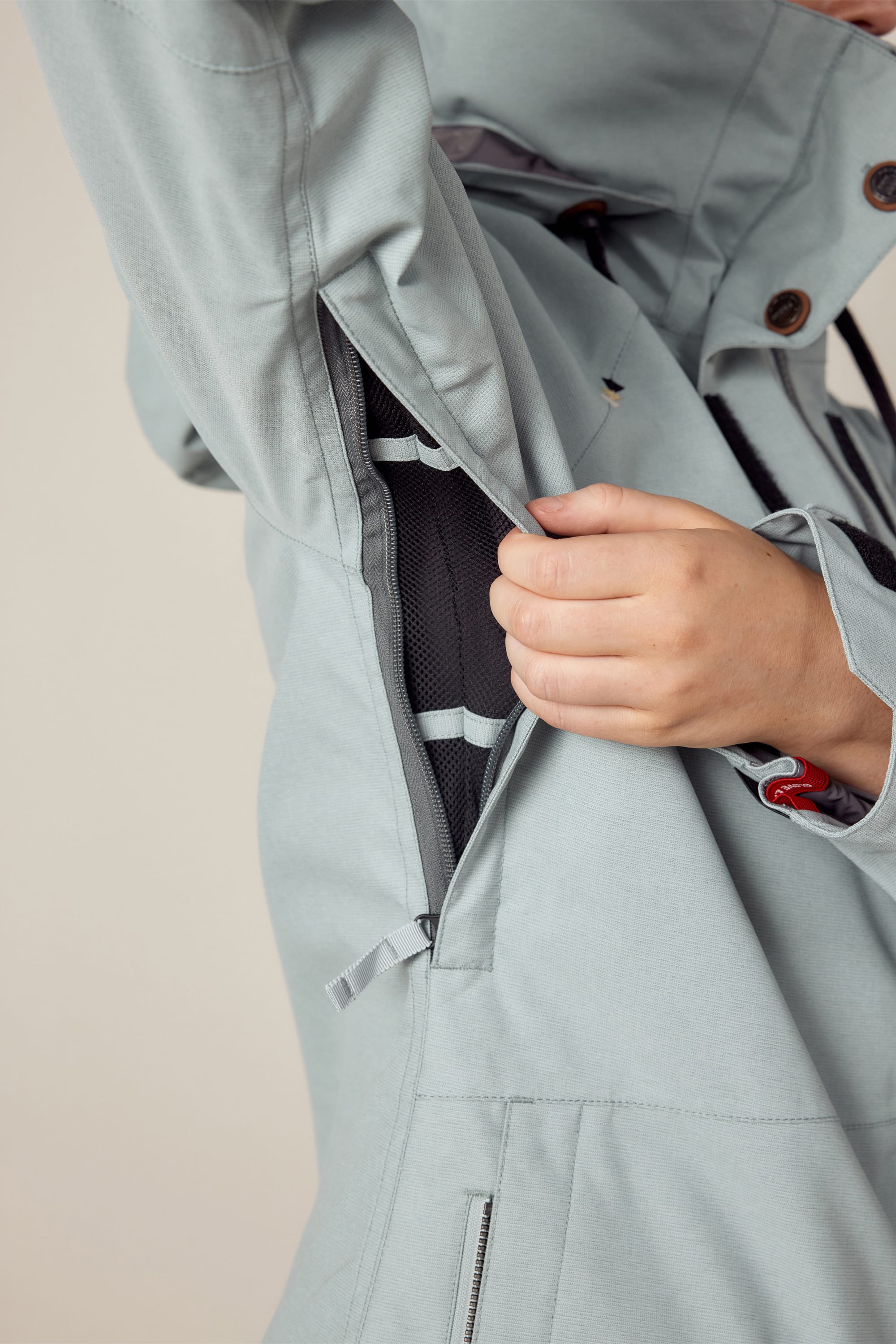 A person opens a zippered vent under the arm of the 686 Womens Smarty 3-In-1 Spellbound Jacket in light gray, revealing black mesh fabric inside.
