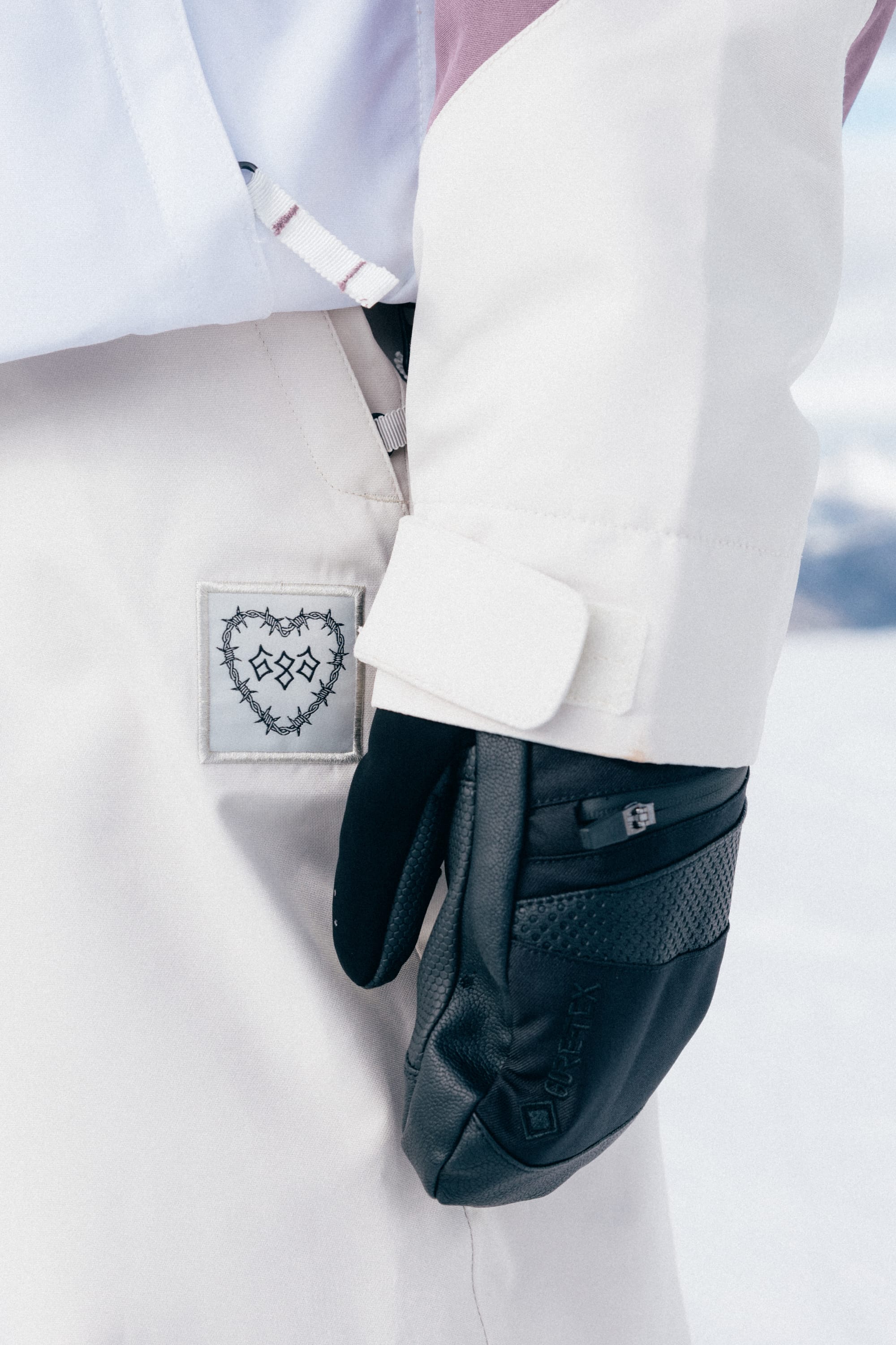 A person wearing the 686 Women’s Outline™ Shell Anorak by 686, along with matching pants and black gloves, standing outdoors in a snowy environment.