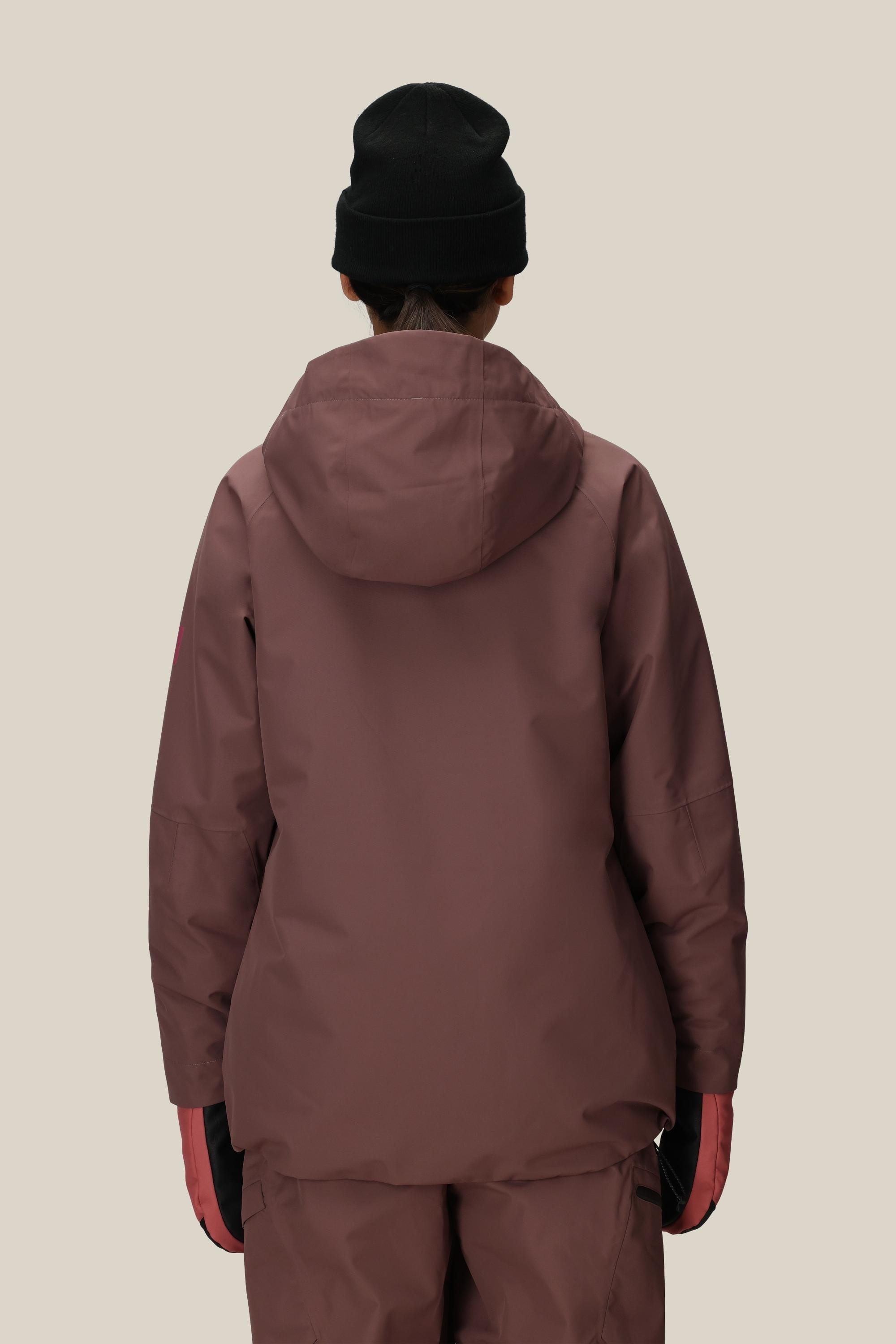 A person is shown from the back against a plain beige background, wearing the 686 Womens Whisper Insulated Jacket in maroon, maroon pants, a black beanie, and pink gloves.