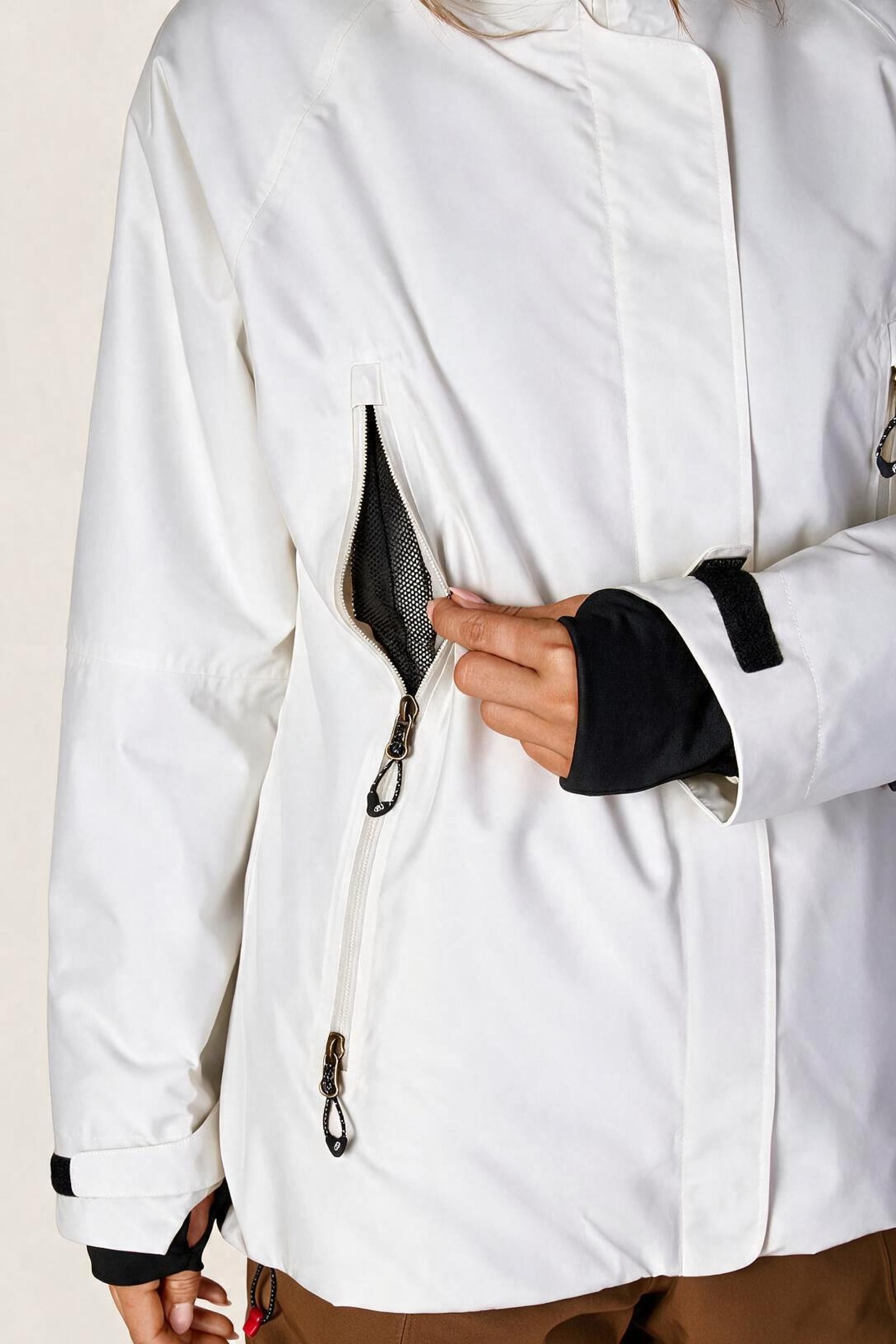 A person wearing the 686 Women’s Whisper™ Insulated Jacket opens a zippered mesh pocket on the front, revealing its interior. Only the lower half of their face and upper body are visible.