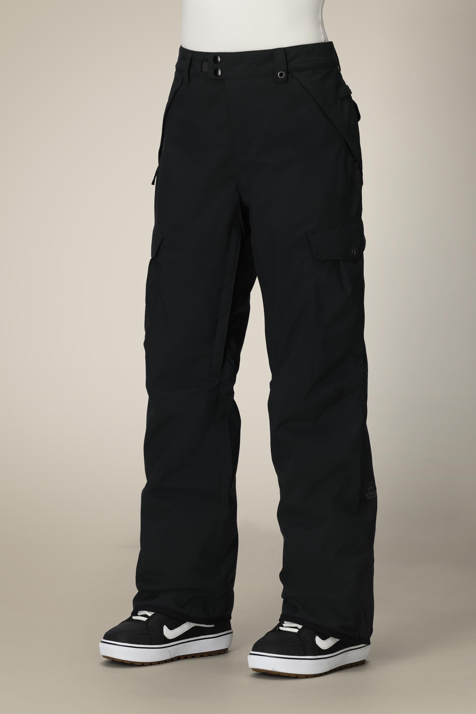 A person wears the 686 Womens Aura Insulated Cargo Pant by 686, featuring side pockets and a relaxed fit, along with black-and-white sneakers, while standing against a plain, light-colored background.