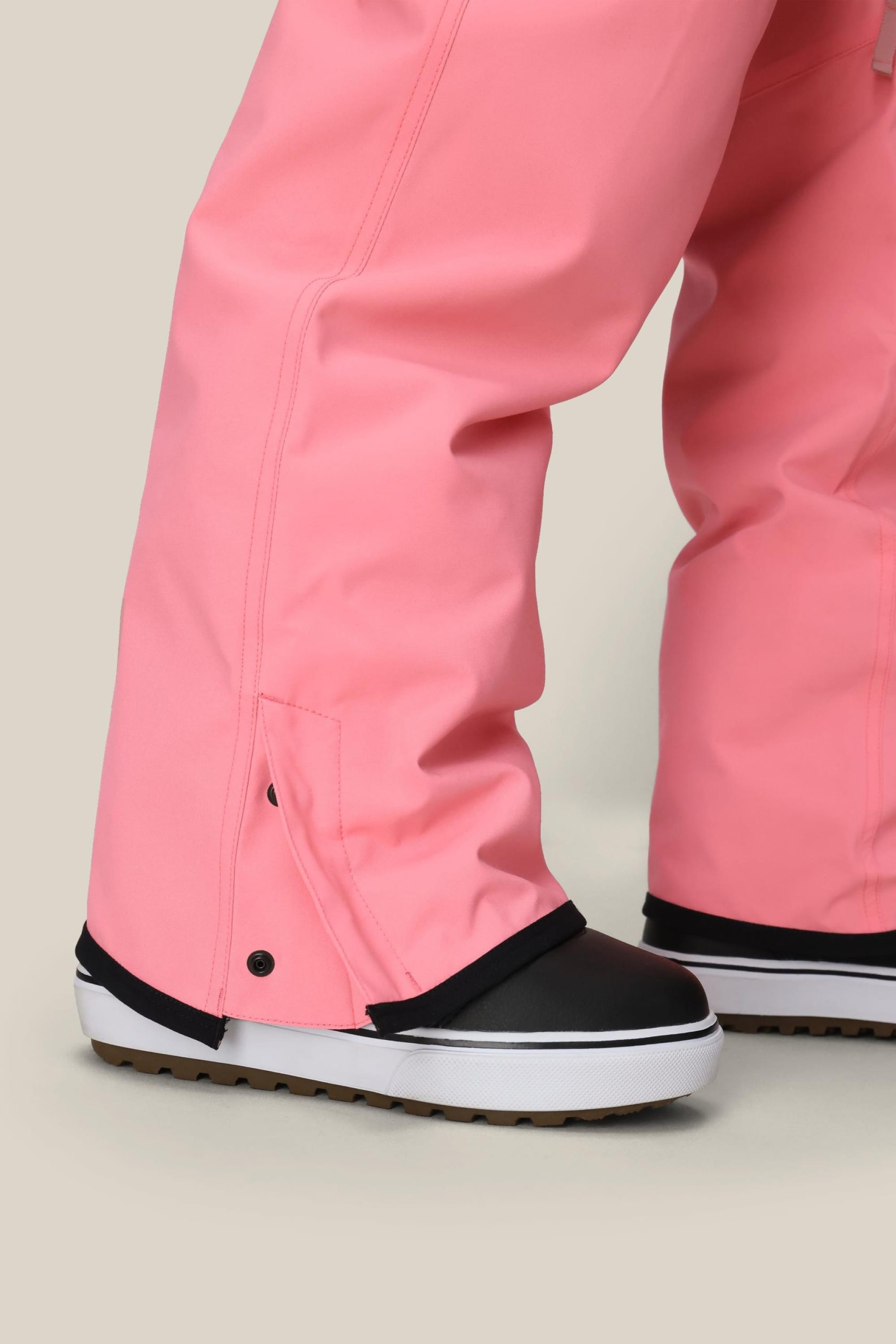 Close-up of a person wearing 686 Womens Aura Insulated Cargo Pant in pink with black-and-white snow boots, shown from the knee down against a plain light background.