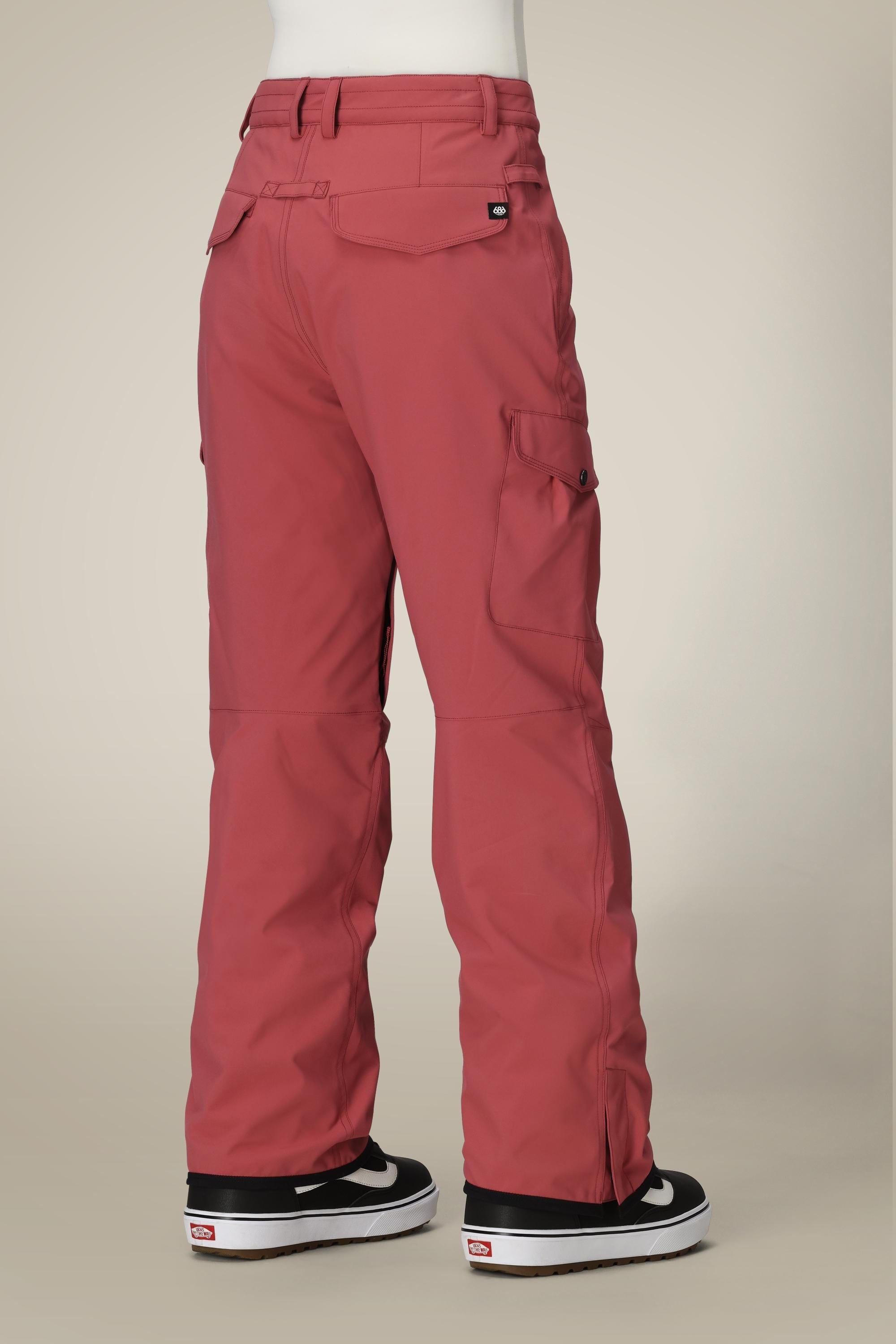 A person is shown from the back against a beige background wearing 686 Womens Aura Insulated Cargo Pant in rose with multiple pockets and black-and-white sneakers.