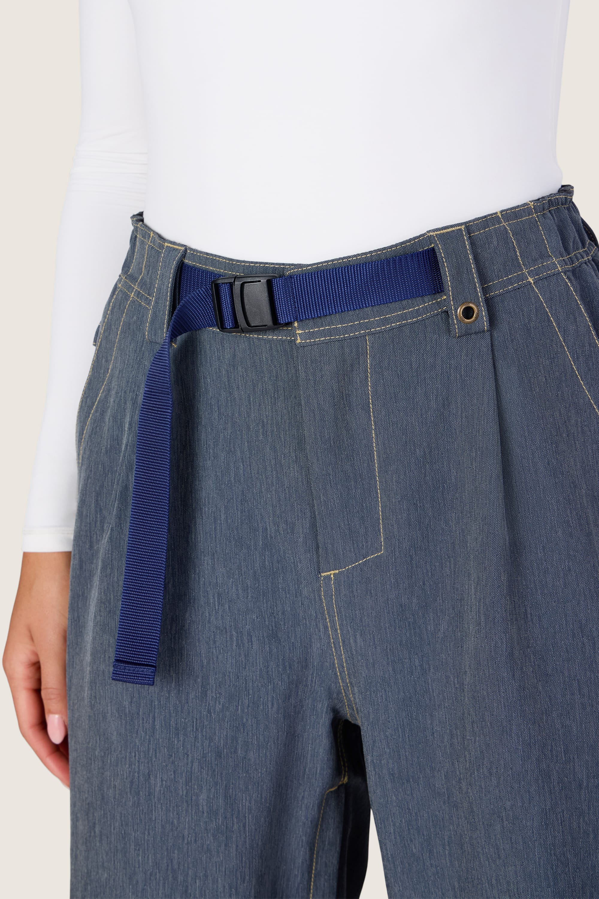 Wearing the 686 Women’s Outline™ Shell Pant by 686, styled with a navy blue fabric belt and a white long-sleeve top. Only the lower torso and one arm are visible.