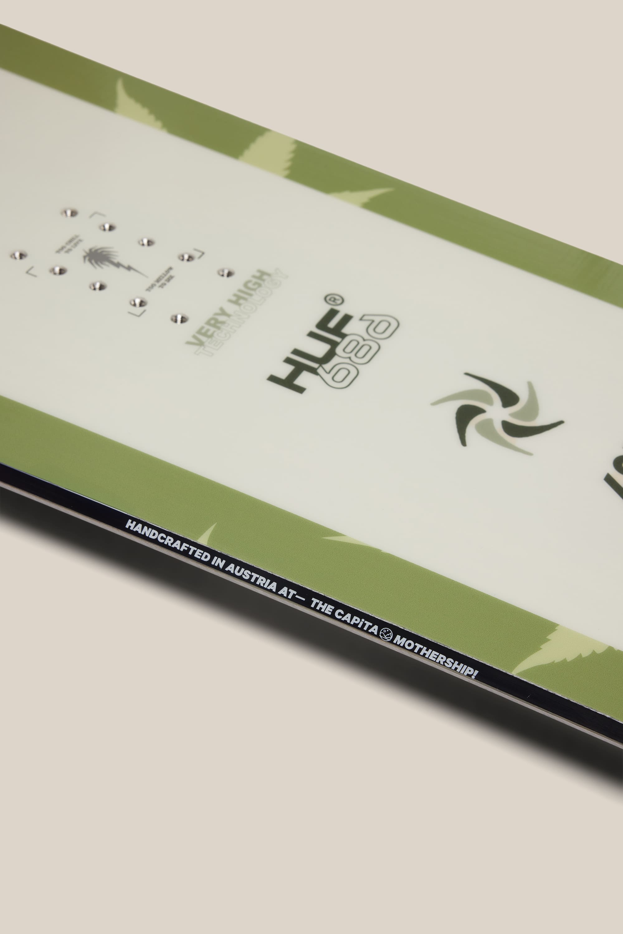 Close-up of the 686 HUF SB Slush Slasher Snowboard in green and white, featuring 686 and HUF logos. Text along the edge reads: HANDCRAFTED IN AUSTRIA AT‚ÄîTHE CAPITA MOTHERSHIP.