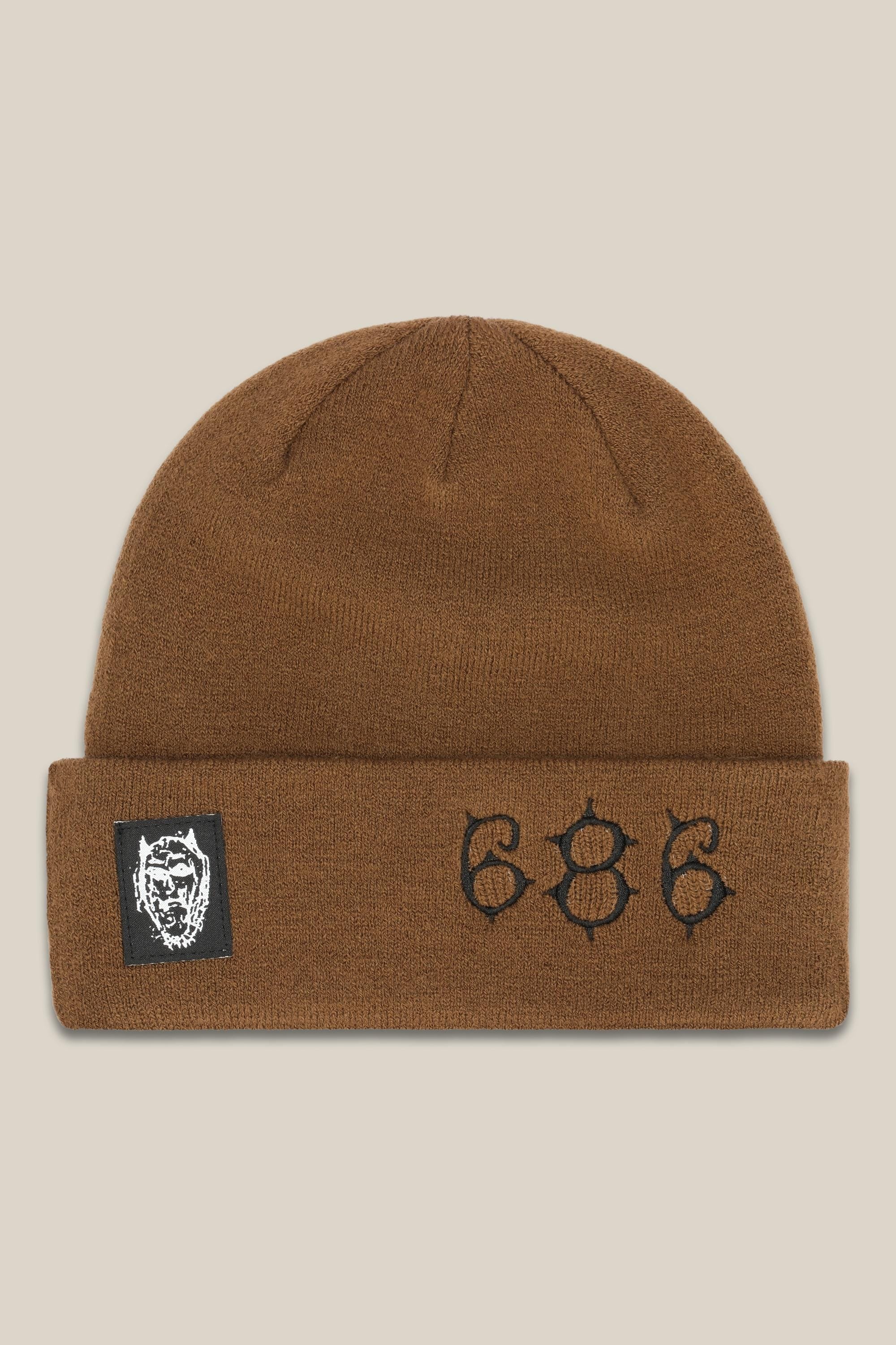 The 686 Cooper Beanie is a brown acrylic knit beanie featuring a black patch with a white graphic on the left and 686 embroidered in black on the folded cuff.