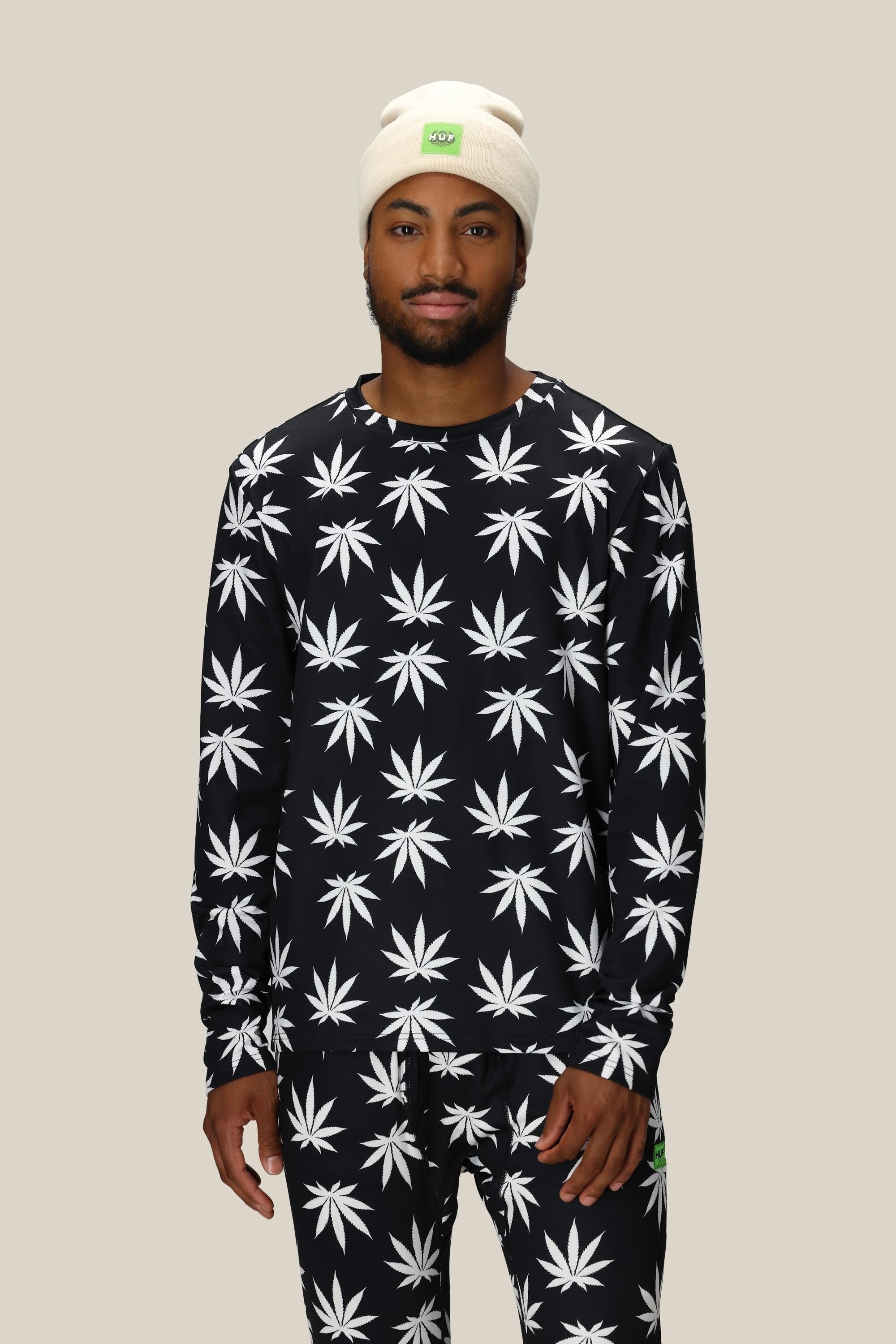 A man wearing the 686 Mens Plantlife Base Layer LS Top, a black polyester top with white leaf prints by 686.