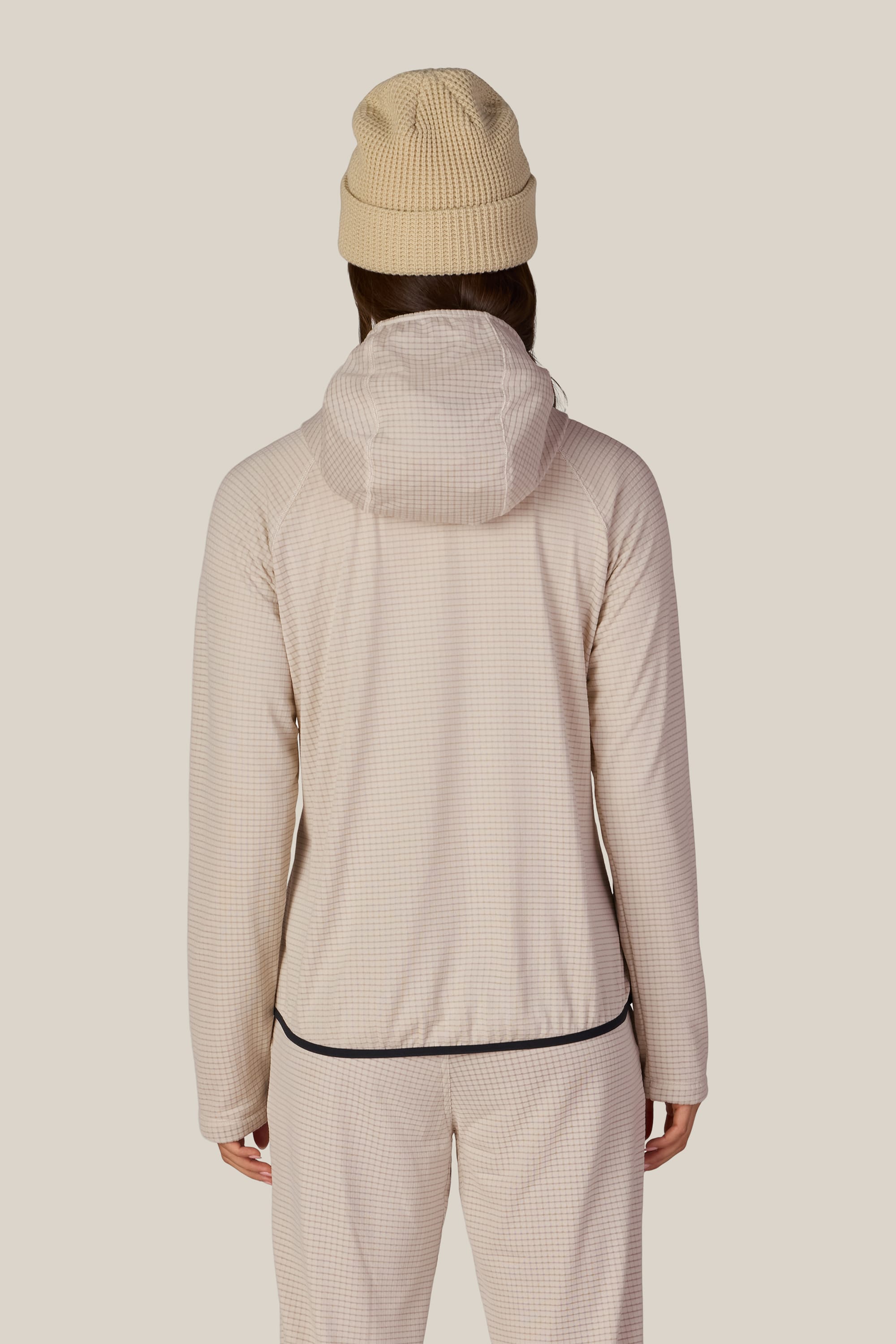 A person facing away, wearing a beige beanie and the 686 Women’s Mission Grid™ Hoody by 686 in a light checkered pattern, paired with matching pants, against a plain light background.