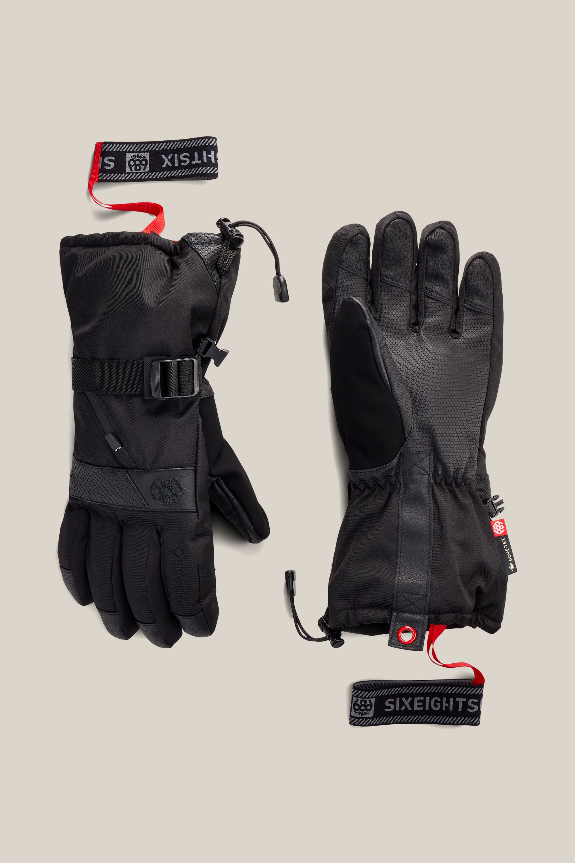 A pair of black 686 Men’s GORE-TEX® SMARTY® 3-In-1 Gauntlet Gloves featuring insulated construction, adjustable straps, wrist loops, and red SIXEIGHTS and HITSIX tags, displayed against a light beige background.