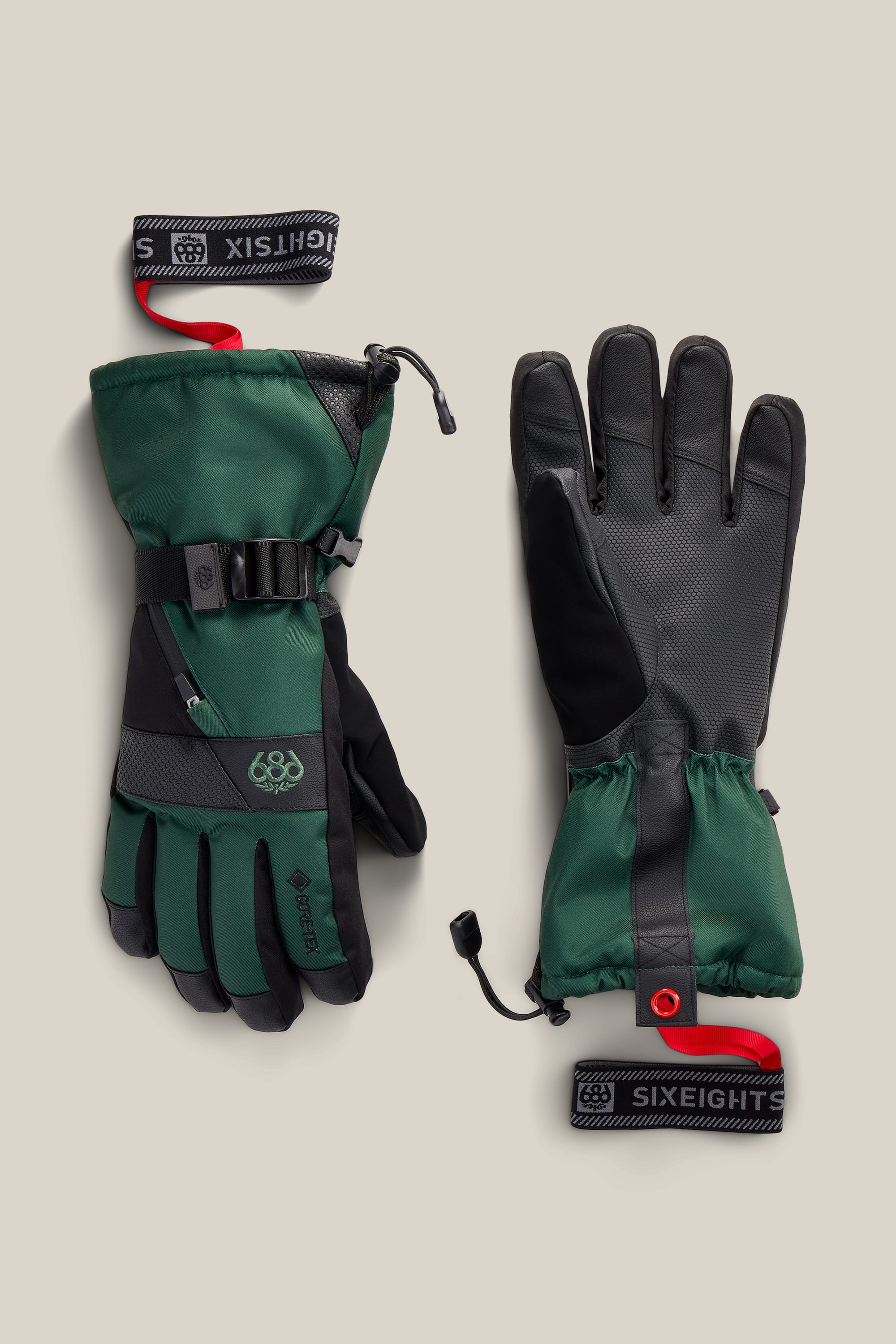 A pair of 686 Men’s GORE-TEX® SMARTY® 3-In-1 Gauntlet Gloves in green and black, featuring wrist straps and adjustable cuffs, shown palm up and palm down on a light beige background.