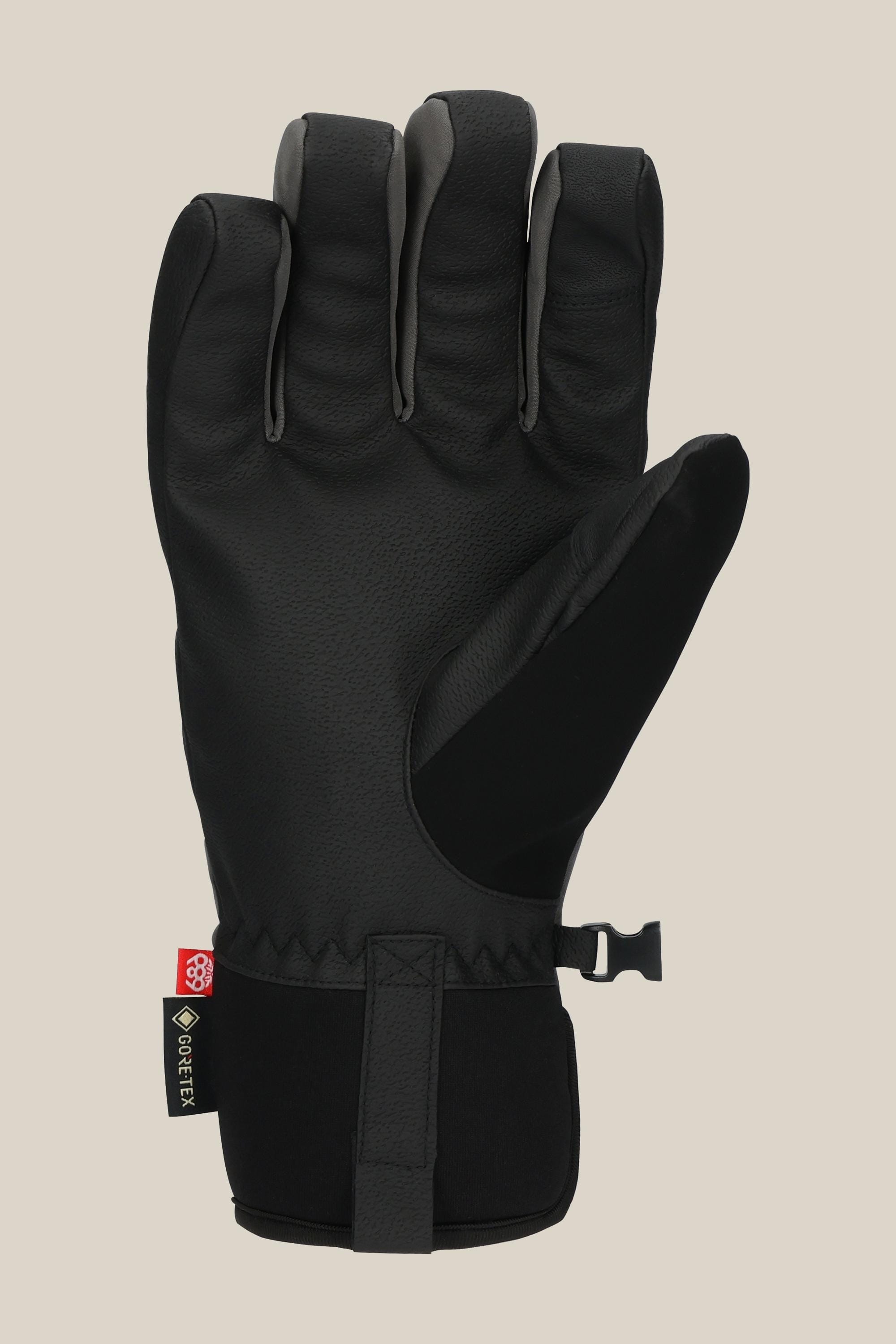 The 686 Mens GORE-TEX Linear Under Cuff Glove by 686 features a black design with textured PU on the palm and fingers, a wrist strap, and a small GORE-TEX tag on the cuff, shown against a plain beige background.