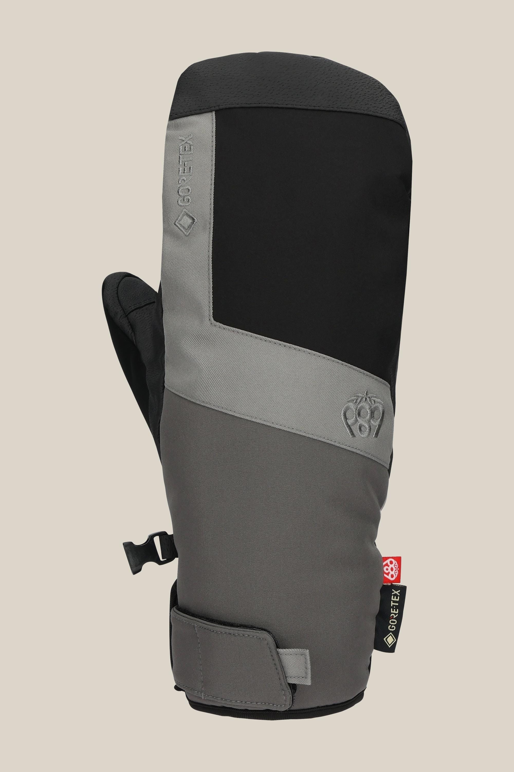 The 686 Mens GORE-TEX Linear Under Cuff Mitt features a black and grey color block design, Velcro wrist strap, Gore-Tex tag, and subtle front branding. Displayed against a plain beige background.