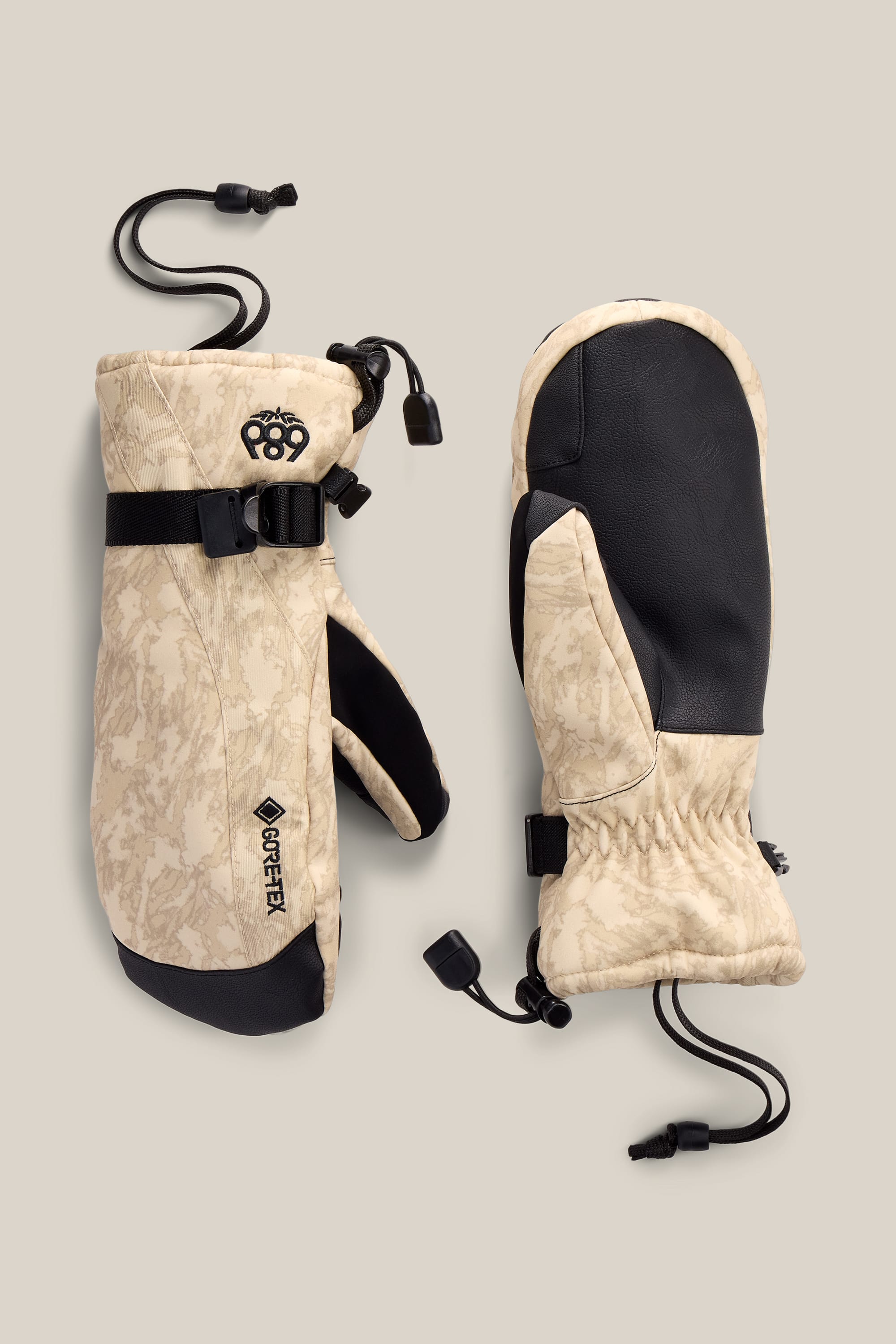 A pair of 686 Women’s GORE-TEX® Linear™ Mitts in beige and black, featuring adjustable straps, GORE-TEX branding, and drawstring closures, displayed on a neutral background.
