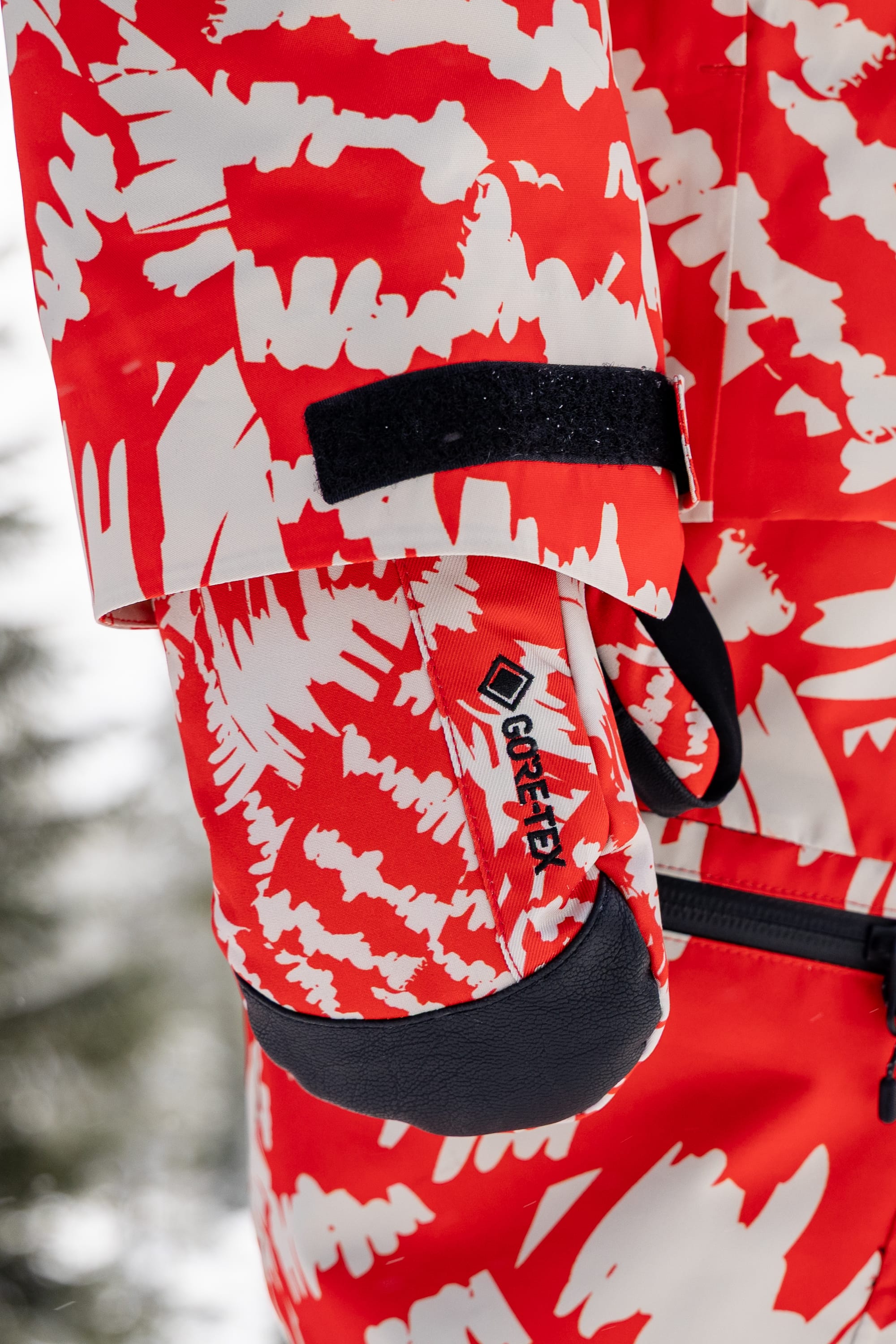 A close-up of a person wearing the 686 Women’s GORE-TEX® Linear™ Mitt by 686, featuring black Velcro on the wrist, outdoors in a snowy setting.