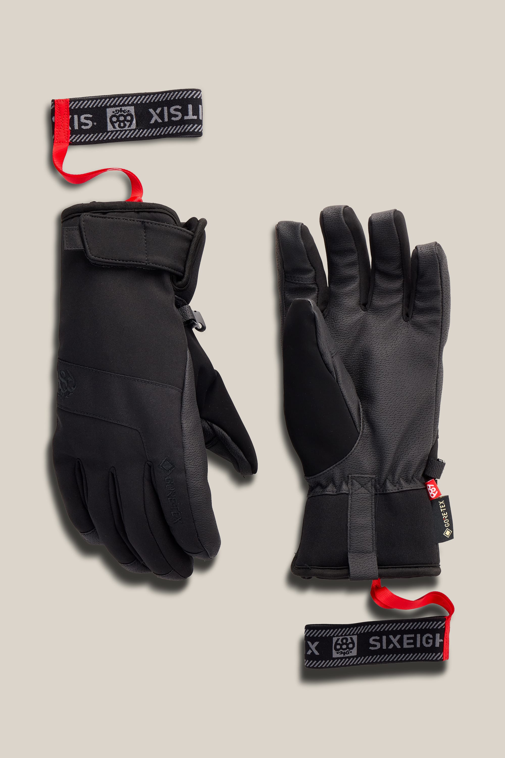 A pair of 686 Women’s GORE-TEX® Linear™ Under Cuff Gloves in black, featuring adjustable wrist straps and red pull tabs, displayed palm up and palm down on a neutral background.