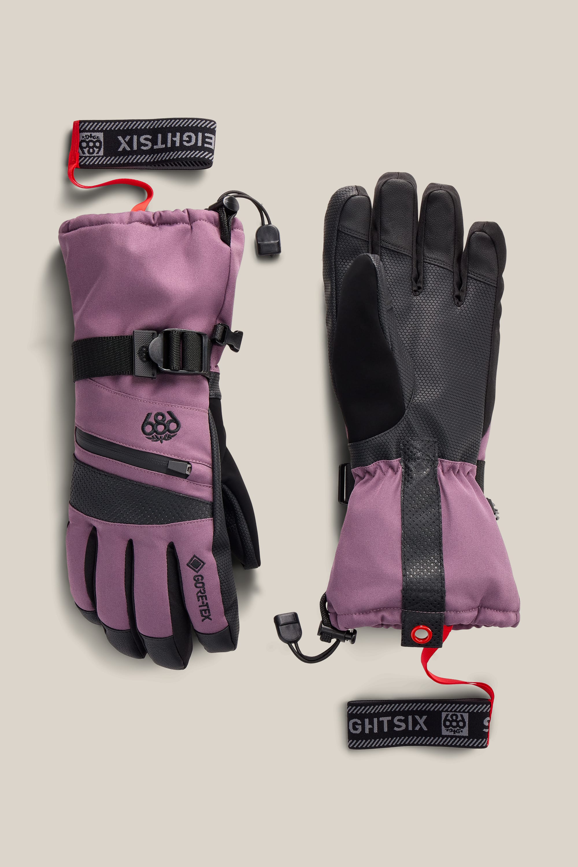 A pair of 686 Women’s GORE-TEX® SMARTY® 3-In-1 Gauntlet Gloves in mauve and black, featuring insulated construction, adjustable cuffs, zippered back pockets, and detachable wrist leashes.