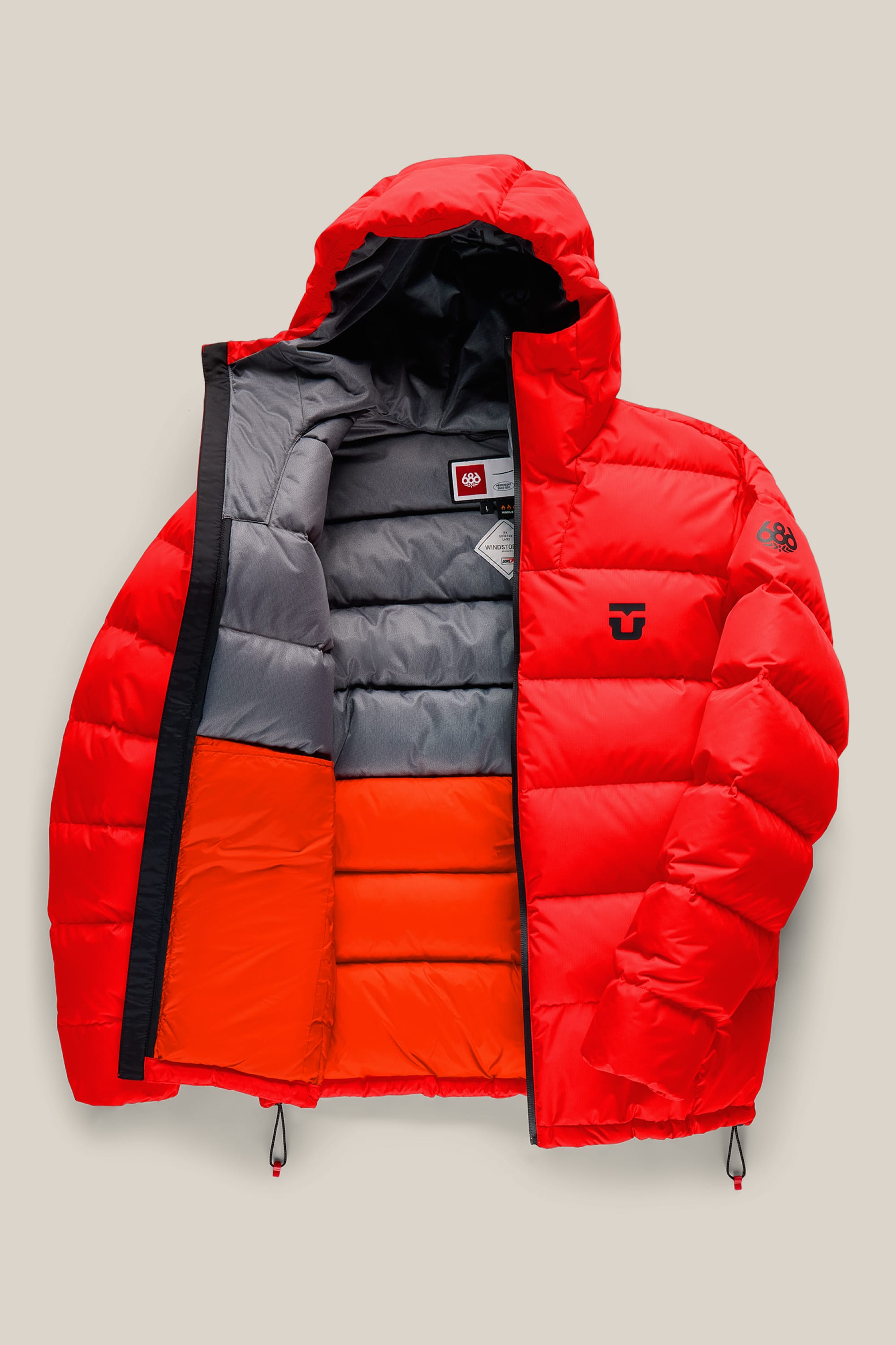 The 686 Men’s WINDSTOPPER® Union Down Puffer Jacket by GORE-TEX® LABS is a red, hooded jacket for men, partially unzipped to reveal a color-blocked gray and orange lining. Black 686 logos appear on the chest and left sleeve. This waterproof puffer features drawstrings at the bottom hem for an adjustable fit.