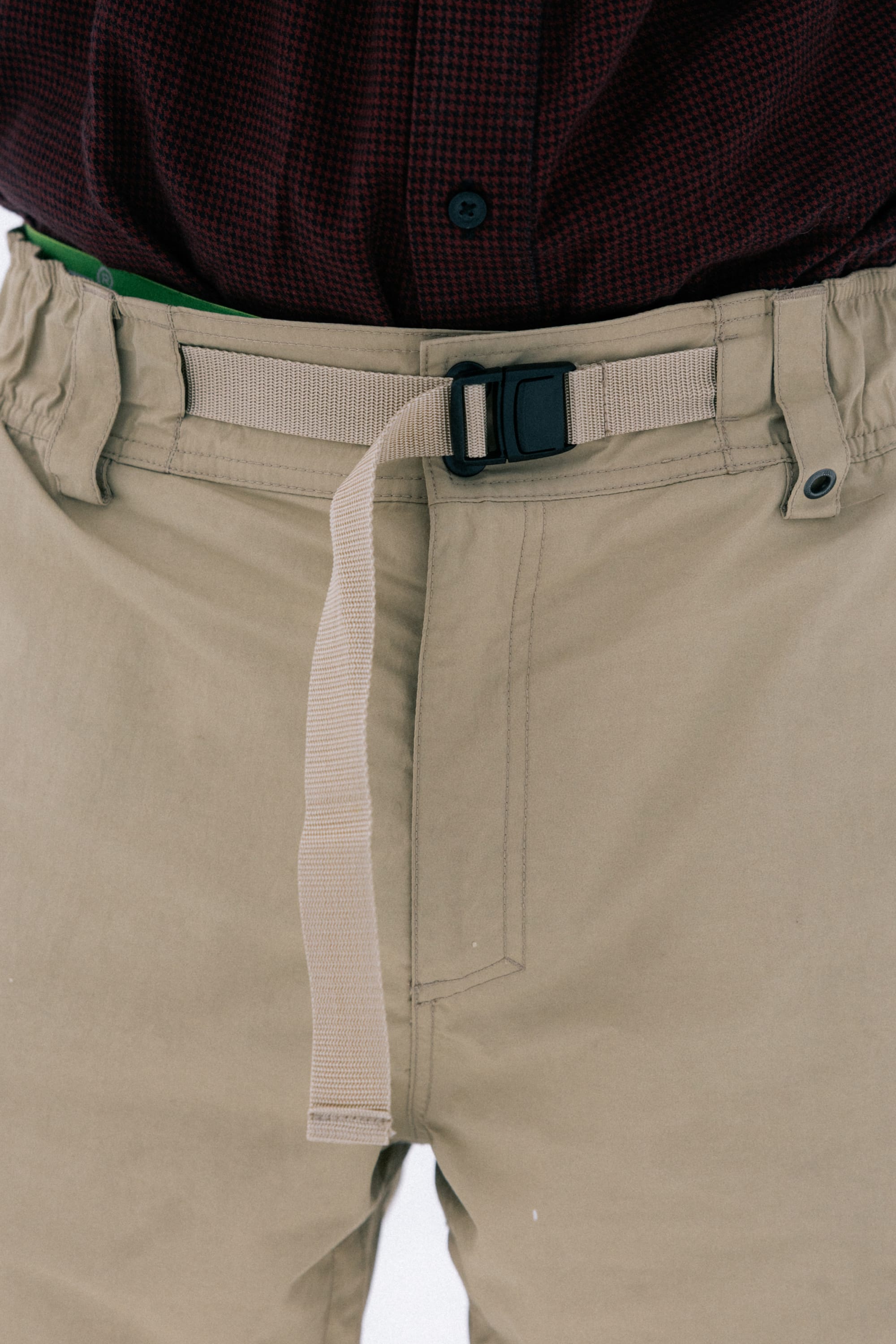 A person wearing the 686 Men’s 686 Dojo® Shell Pant in beige, styled with a beige nylon belt featuring a black plastic buckle and an excess strap hanging down the front, paired with a maroon button-up shirt.