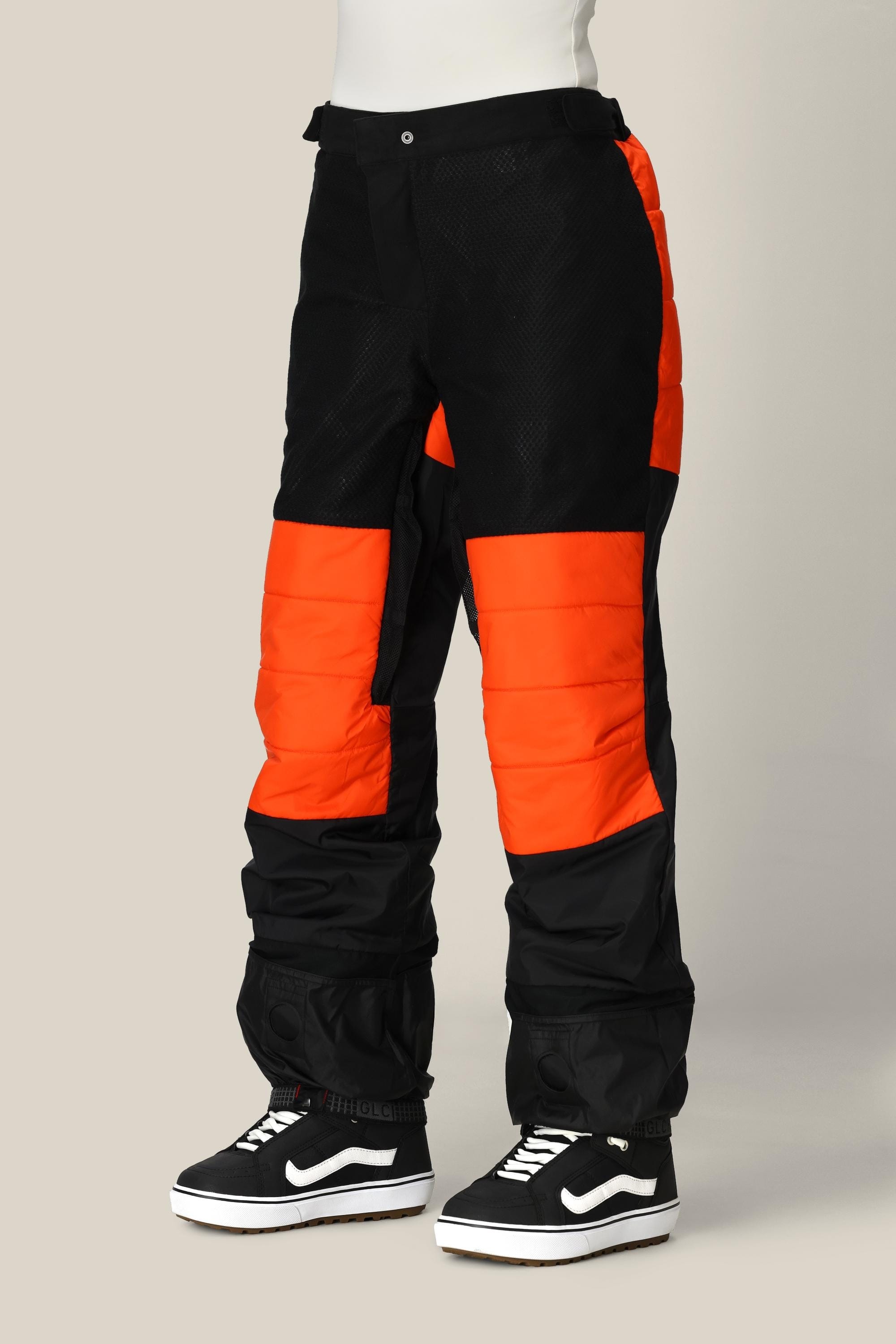 A person is shown from the waist down against a plain background, wearing the 686 Women’s Geode Thermagraph® Pant—black and bright orange color-block cargo pants crafted from waterproof polyester—paired with black-and-white Vans sneakers.