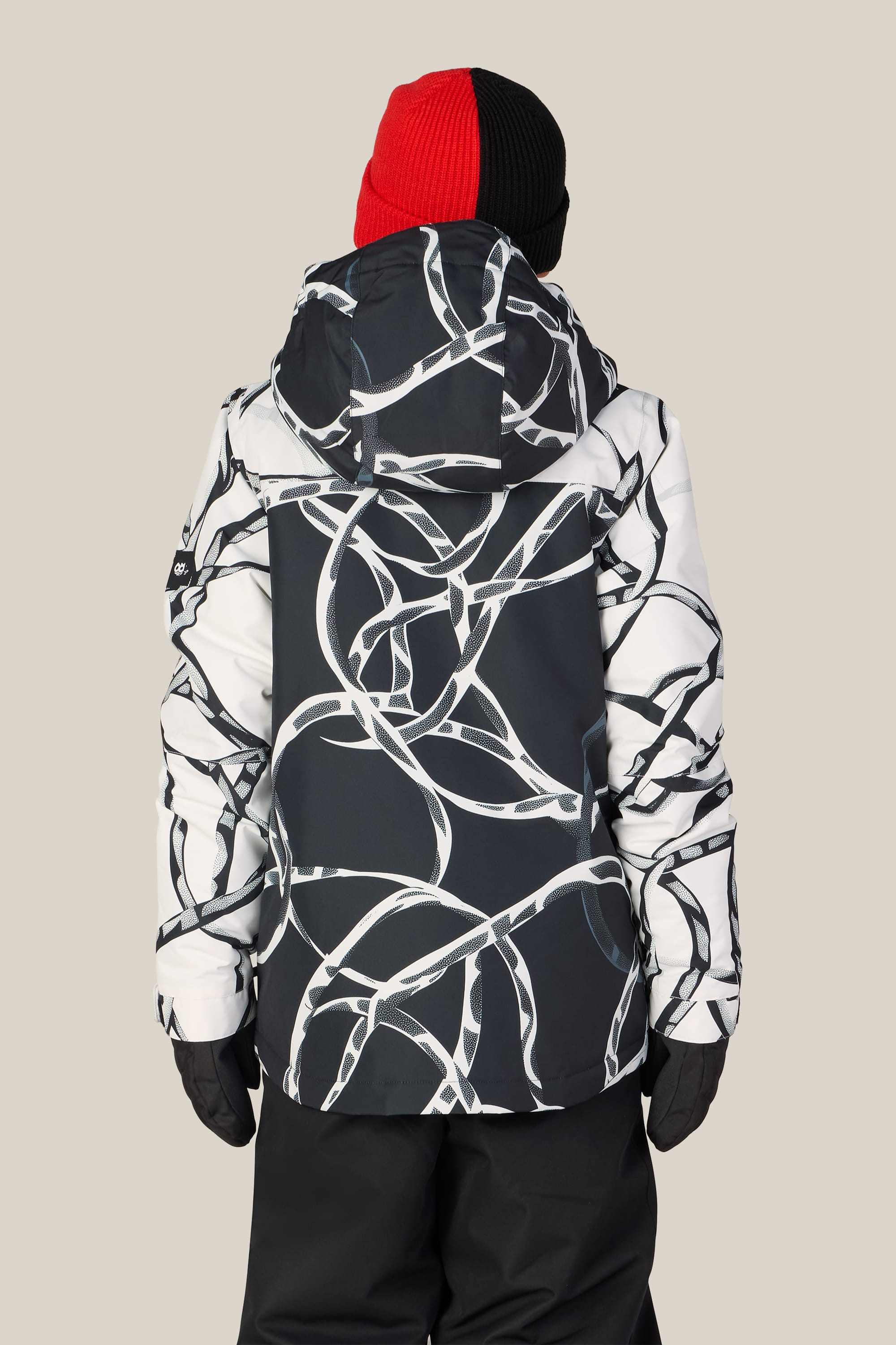 A person is wearing the 686 Boys’ Gateway™ Insulated Jacket by 686—a black and white abstract-patterned polyester boys jacket—paired with black pants, black gloves, and a red-and-black beanie, standing facing away from the camera against a plain background.