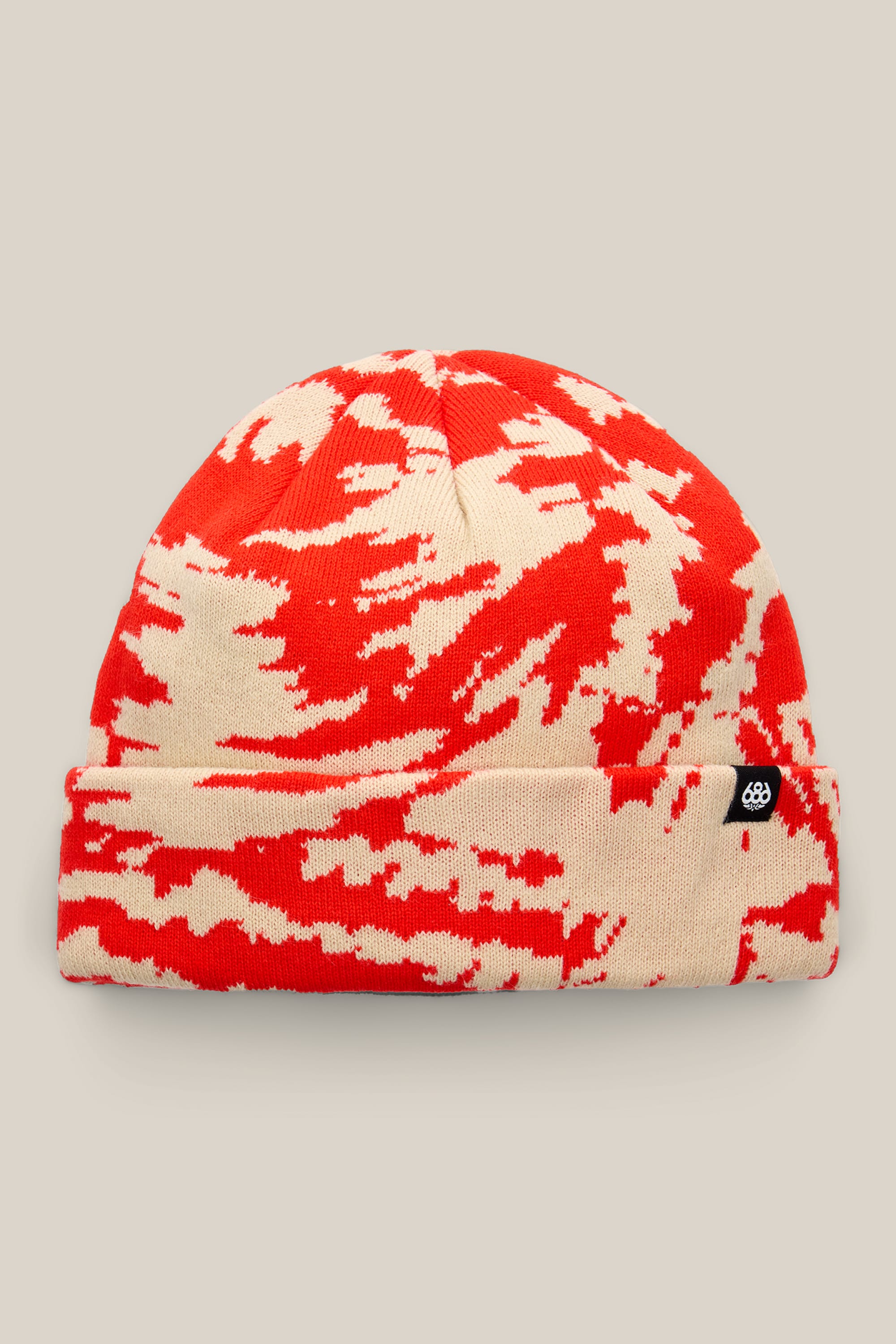 The 686 Reverb Beanie by 686 is made from acrylic knit and showcases a red and beige abstract pattern, finished with a small black tag on the cuff, presented against a neutral background.